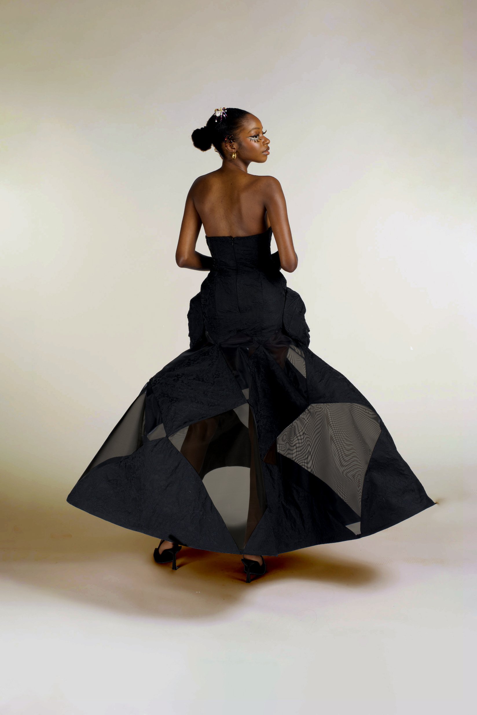 A woman wearing a strapless black dress with a voluminous, textured skirt, standing against a neutral background.