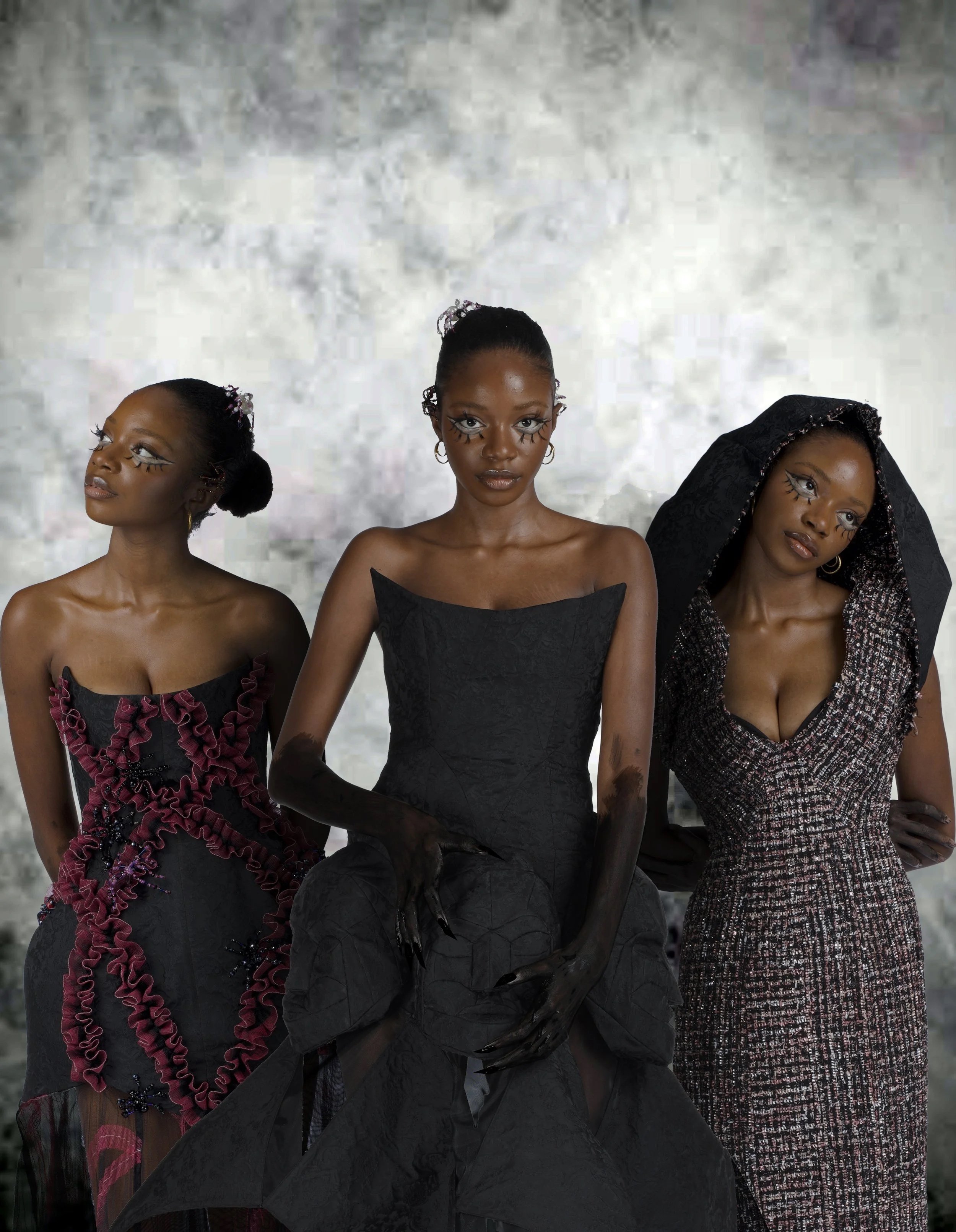Three women dressed in high fashion black and maroon outfits with dramatic makeup and accessories, posing against a textured background.