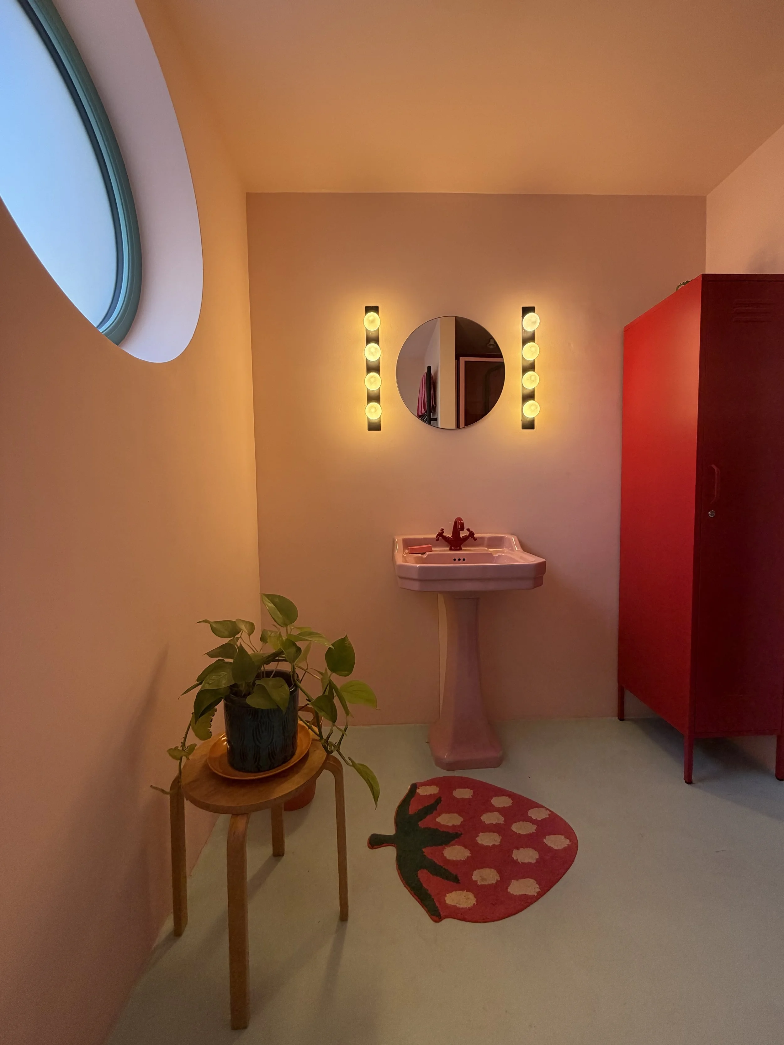 Pink bathroom inside Cloud House with a pedestal basin, circular mirror and bold red details