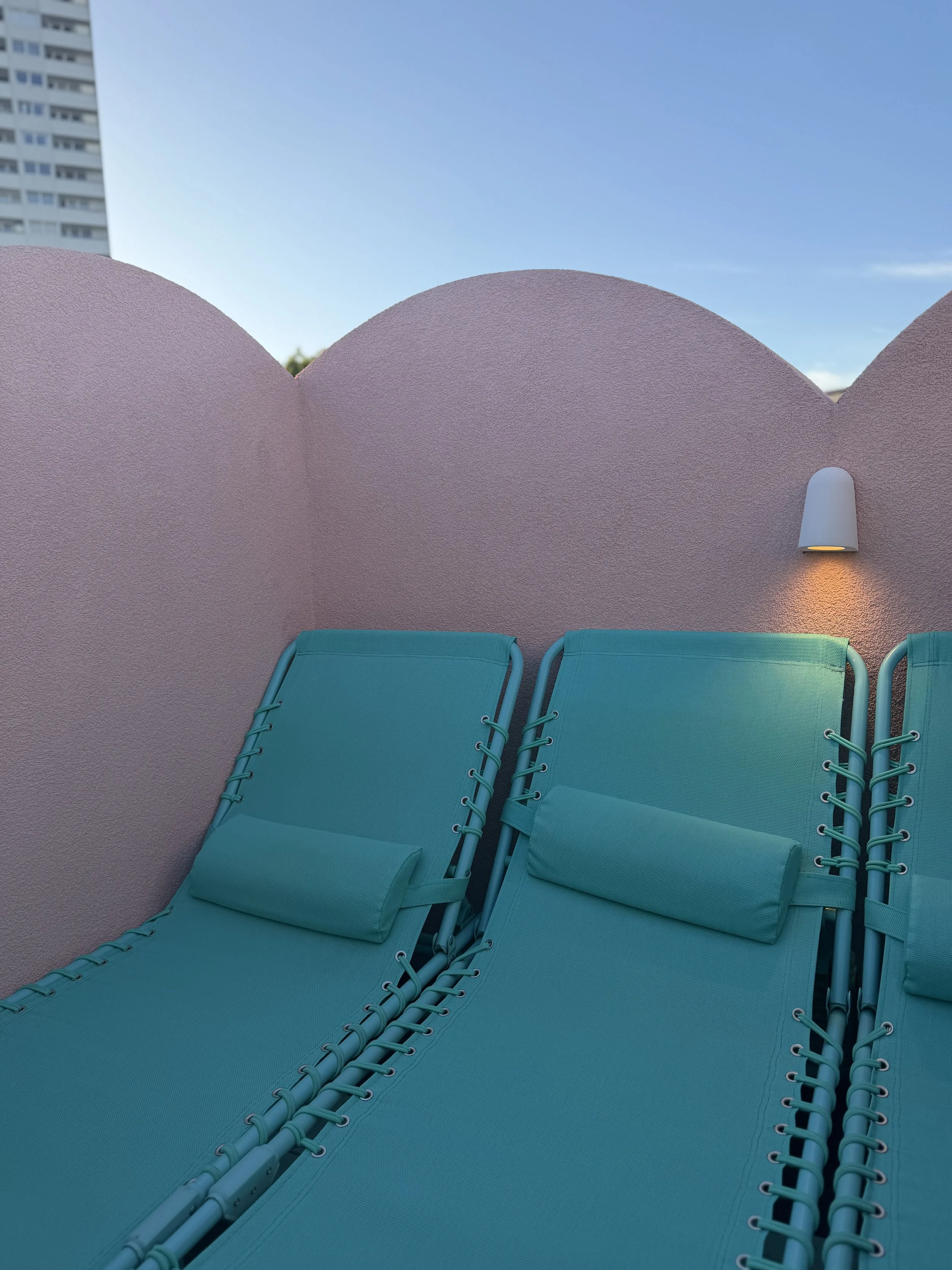 Turquoise sun loungers against the scalloped pink walls of the Cloud House rooftop terrace