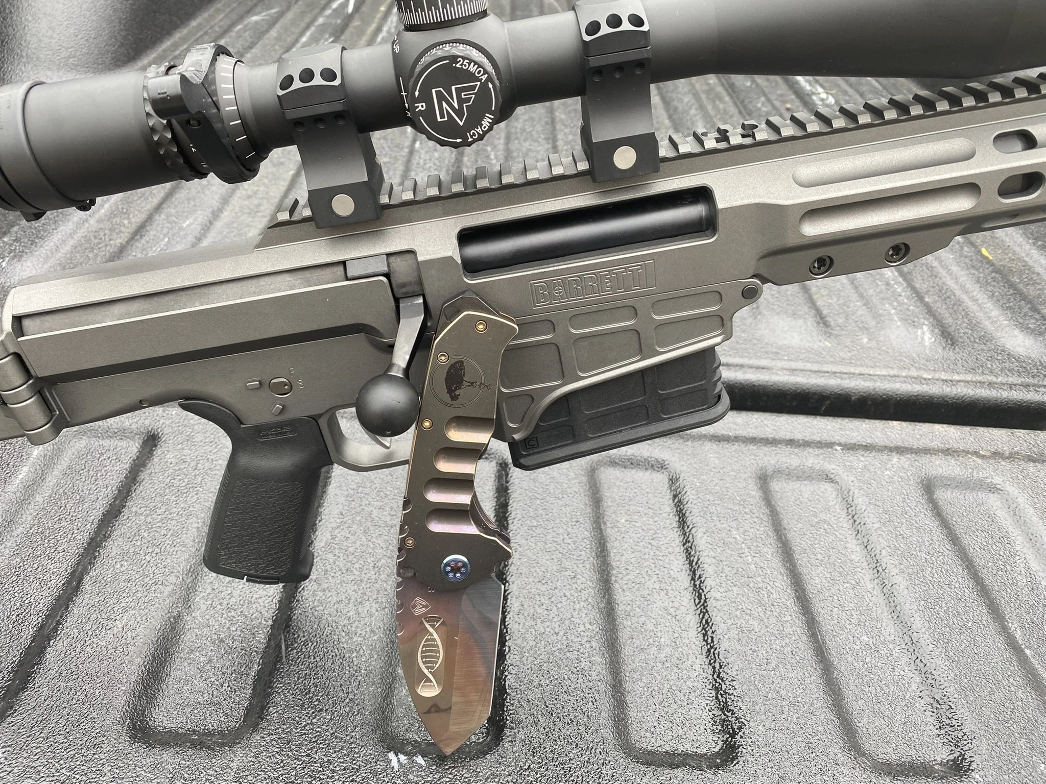A Barret MRAD with a Medford Knife and Tool Praetorian TI knife, resting on a truck bed liner.
