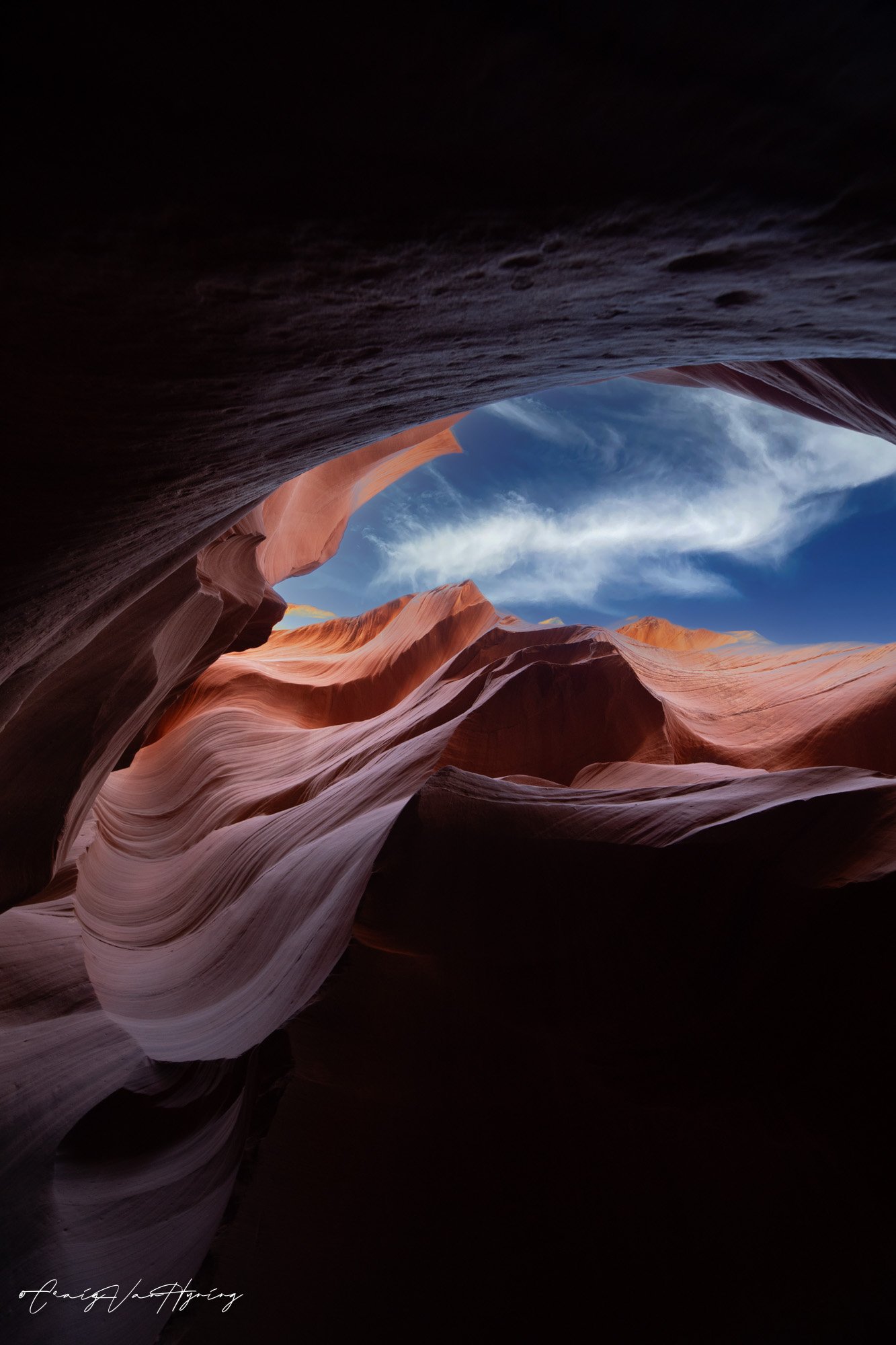View of a canyon with smooth, layered orange and pink rock formations under a blue sky with white clouds.