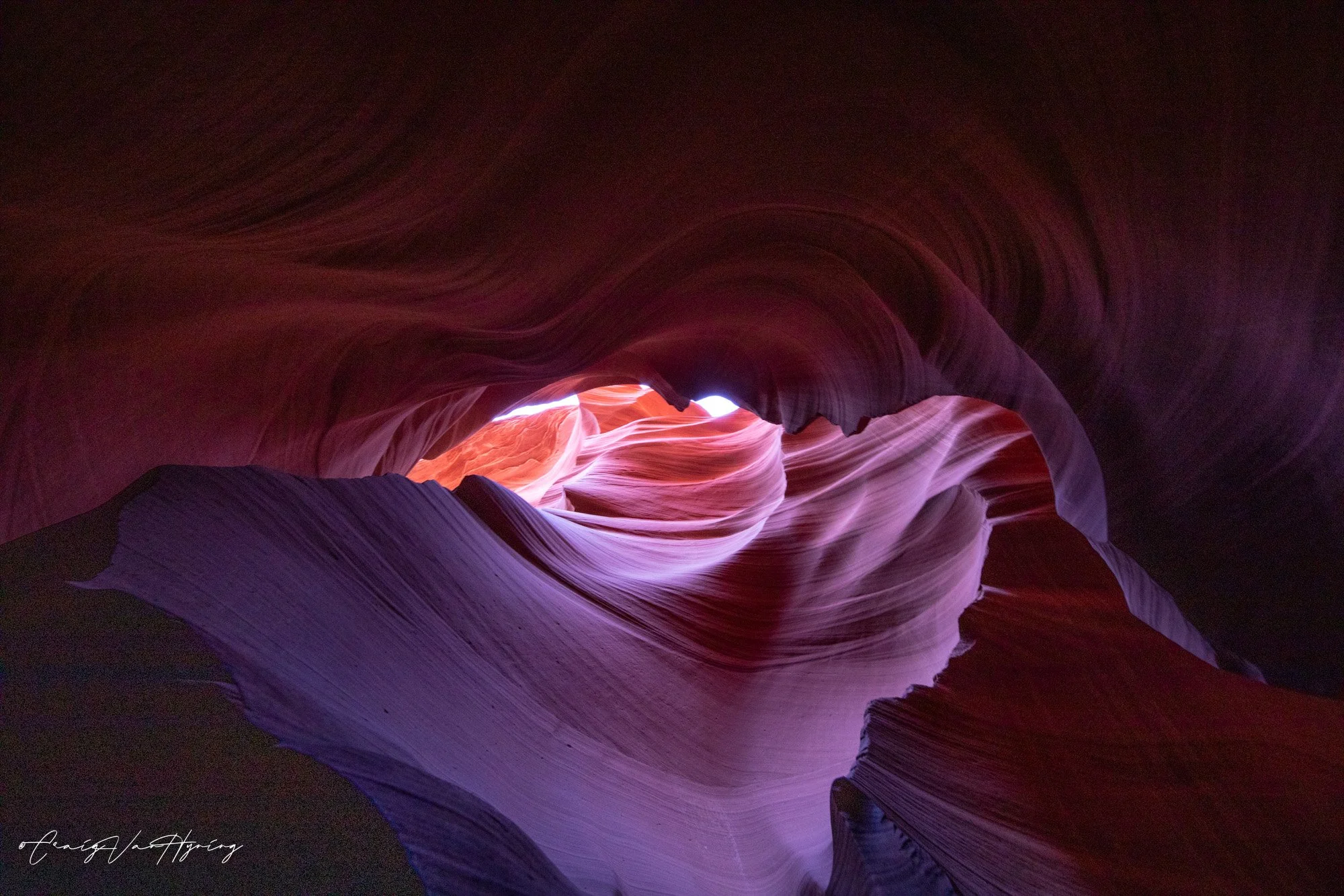 Smooth, curved rock formations inside a narrow slot canyon, with sunlight shining through from above.