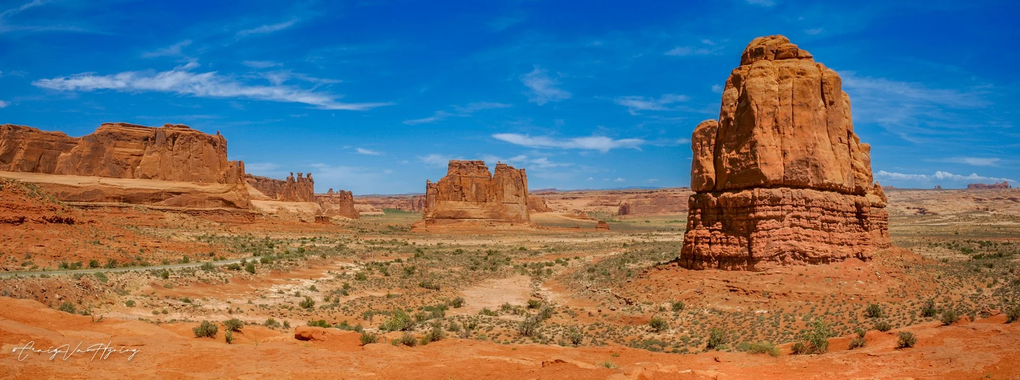A desert landscape with large red sandstone rock formations under a blue sky with some clouds.