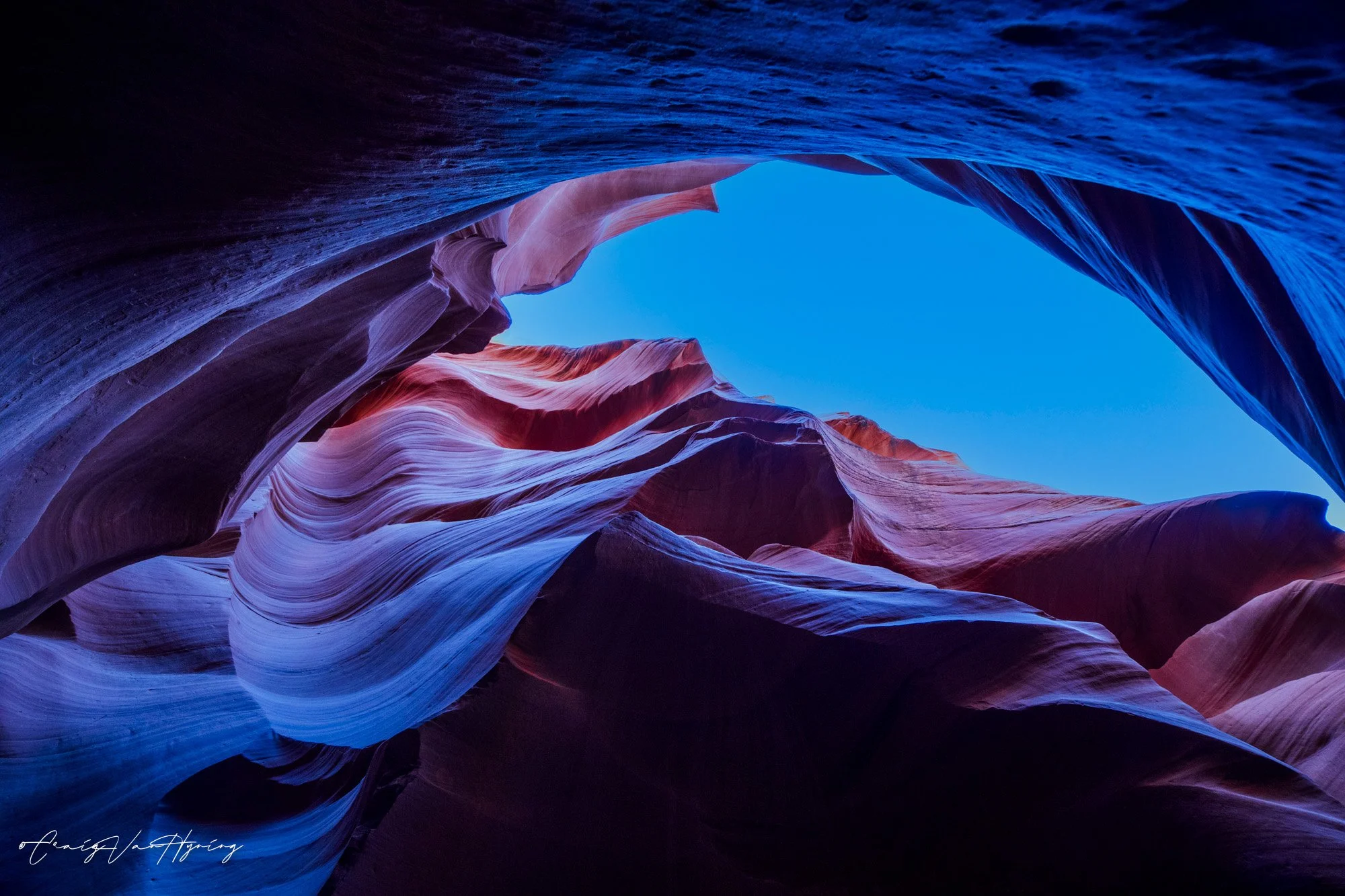 A colorful view of Antelope Canyon showing swirling rock formations and a bright blue sky visible at the top.