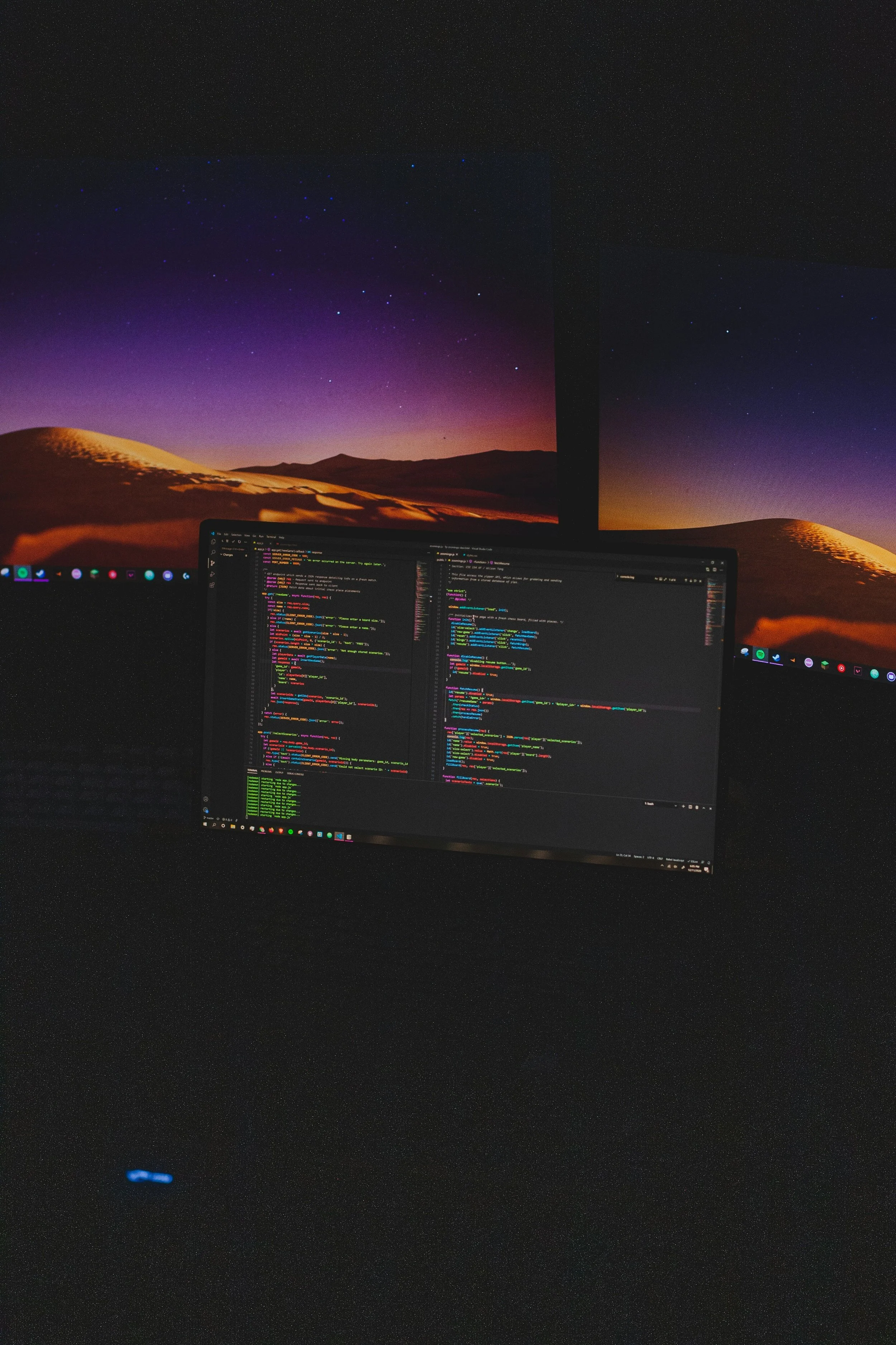 A dual-monitor computer setup with a code editor open on the screen, set against a background of a starry desert landscape at dusk.