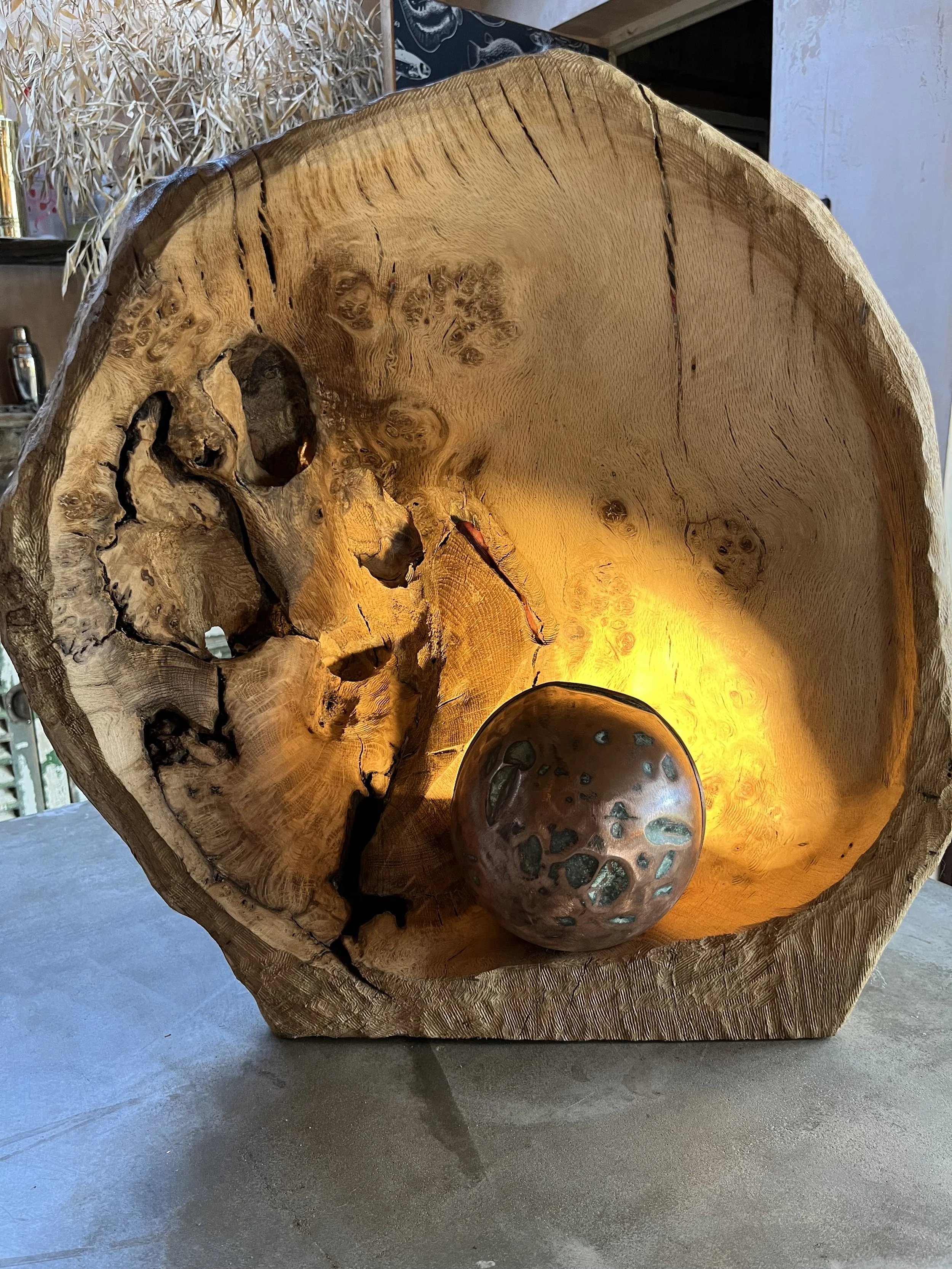 A decorative wooden bowl with a hollowed-out interior, a light source illuminating the inside, and a small ceramic or stone sphere resting inside.