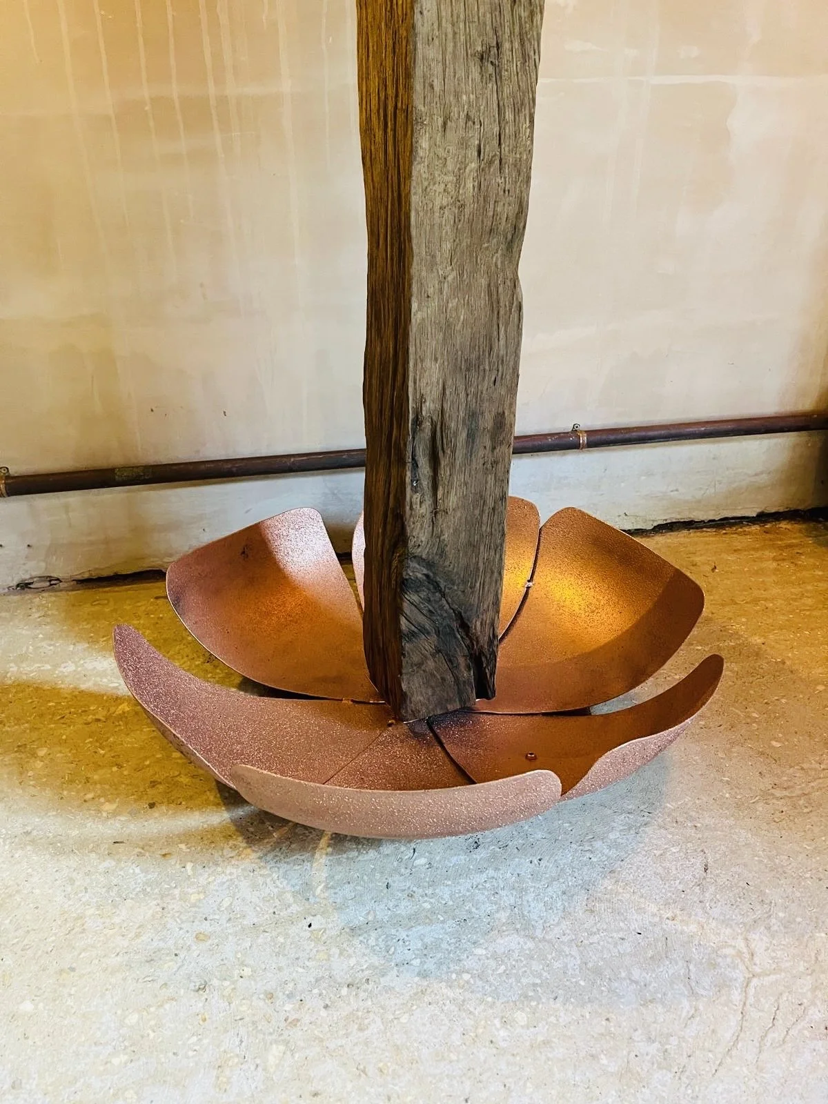 A wooden post standing in a metal flower-shaped basin on a concrete floor.