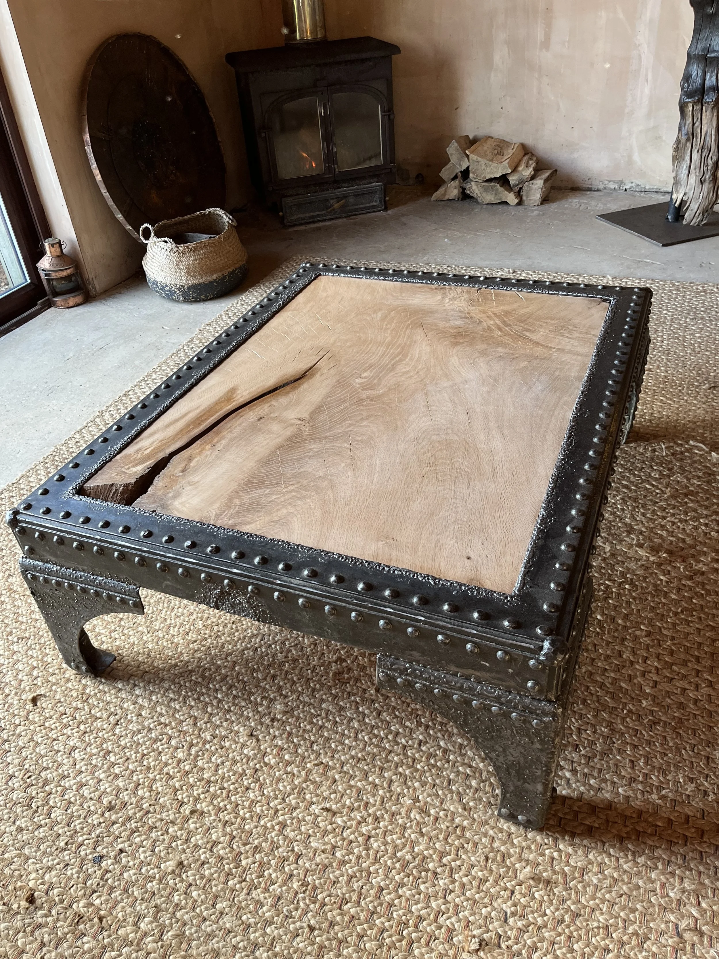 A rustic coffee table with a wooden top and metal riveted frame in a cozy living room.