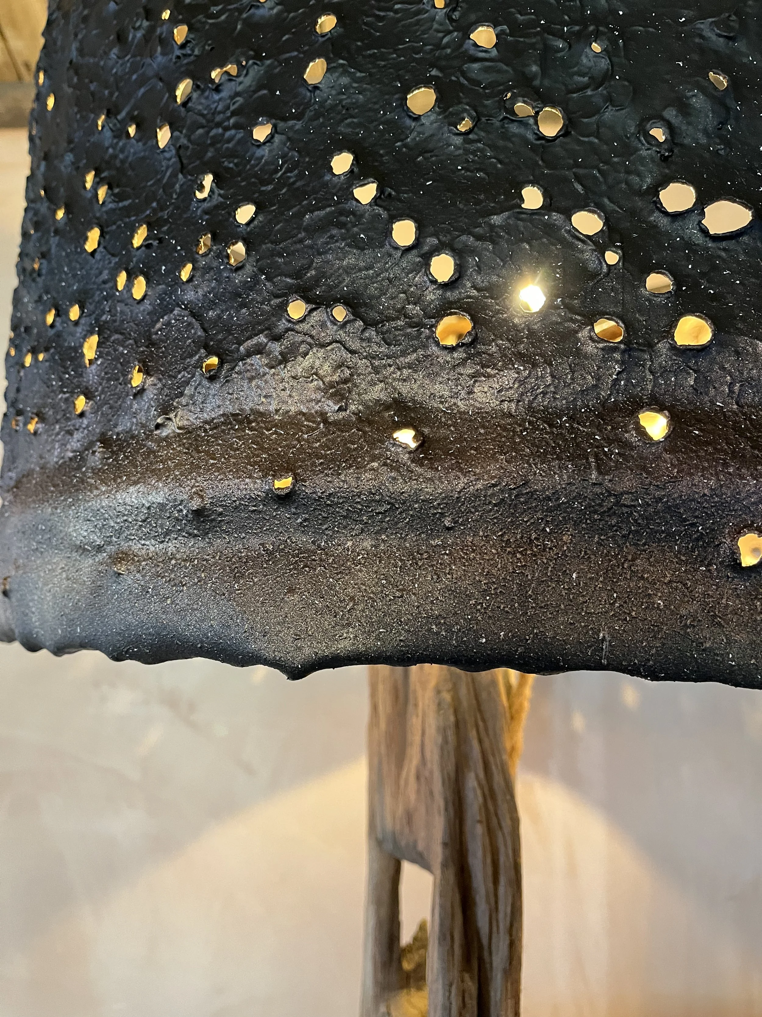 Close-up of a black, perforated, textured metal lampshade with light shining through holes, mounted on a wooden stand.