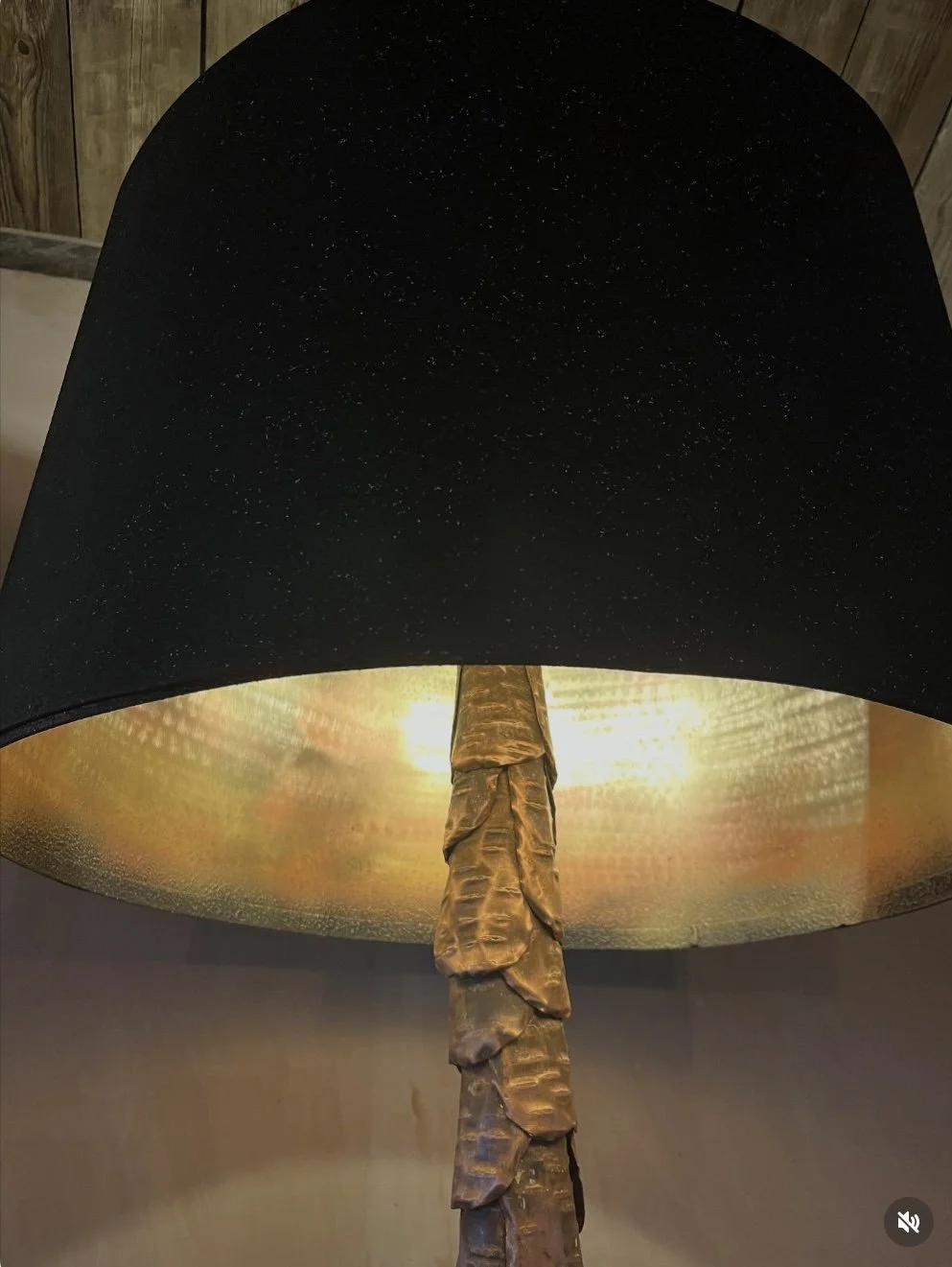Close-up of a table lamp with a black lampshade and a textured, gold-colored base.