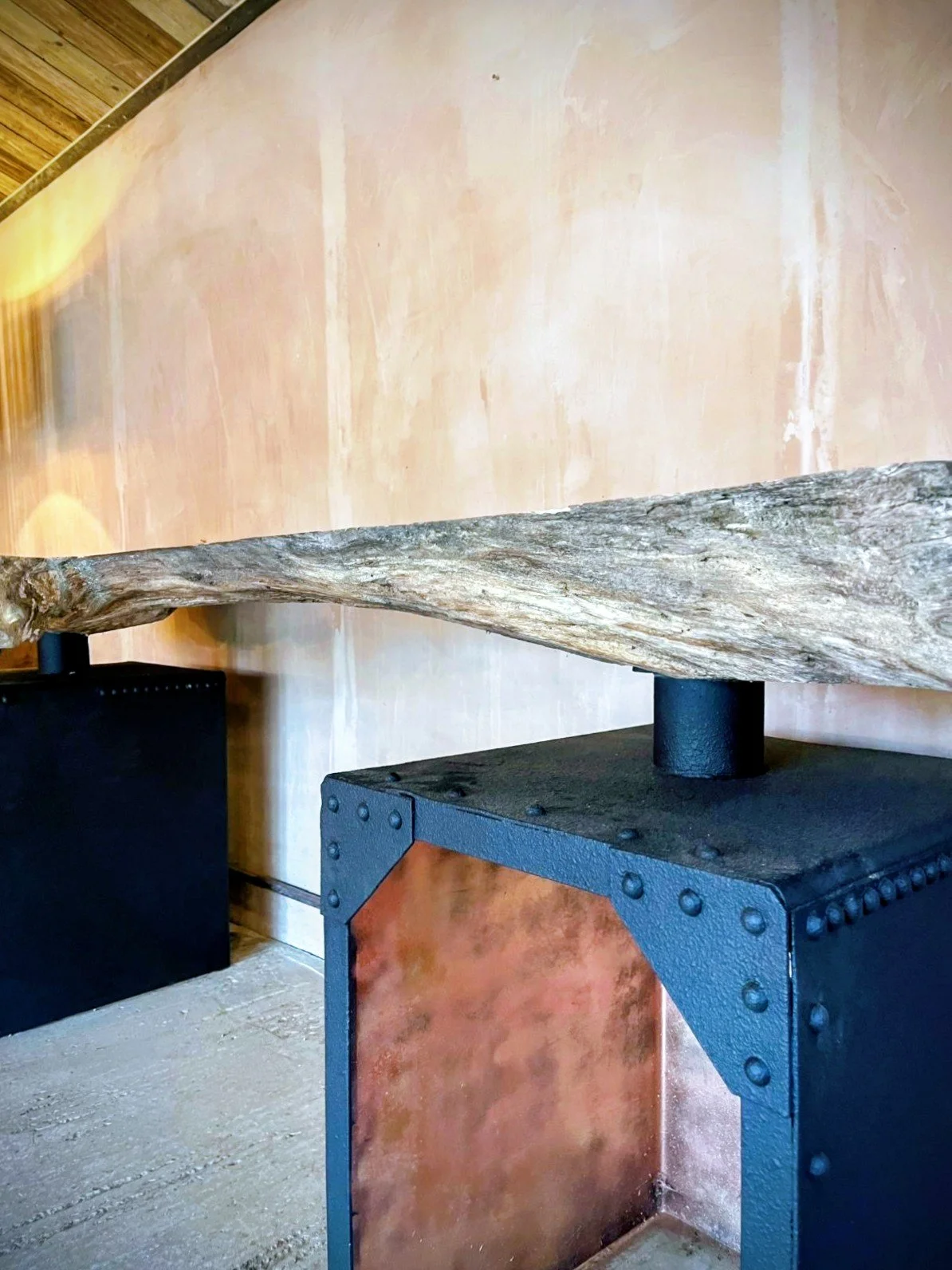 A rustic wooden beam resting on a black metal stand in front of a textured tan wall.