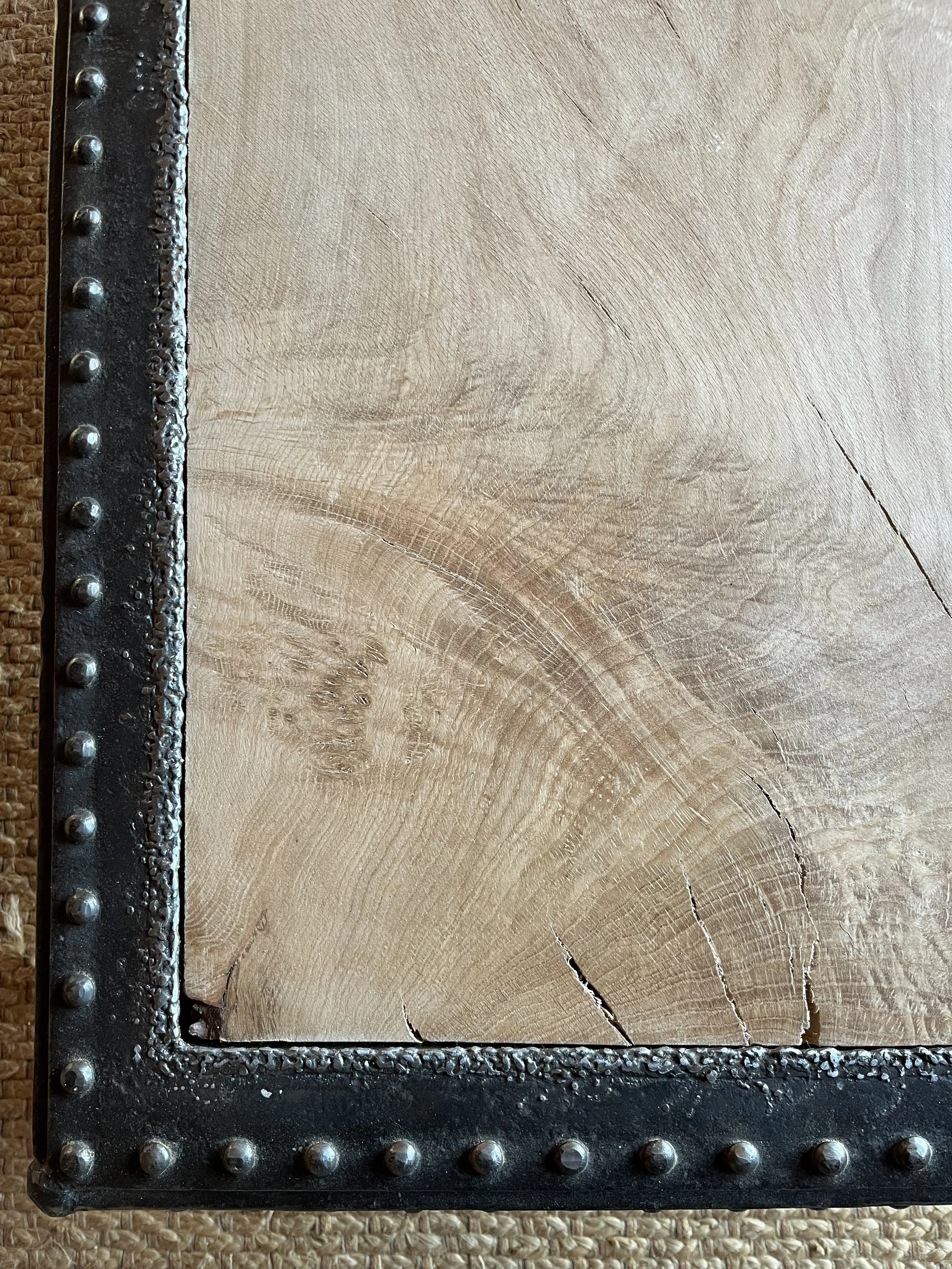 Close-up of a wooden table with a metal riveted frame, showing the natural wood grain and cracks.