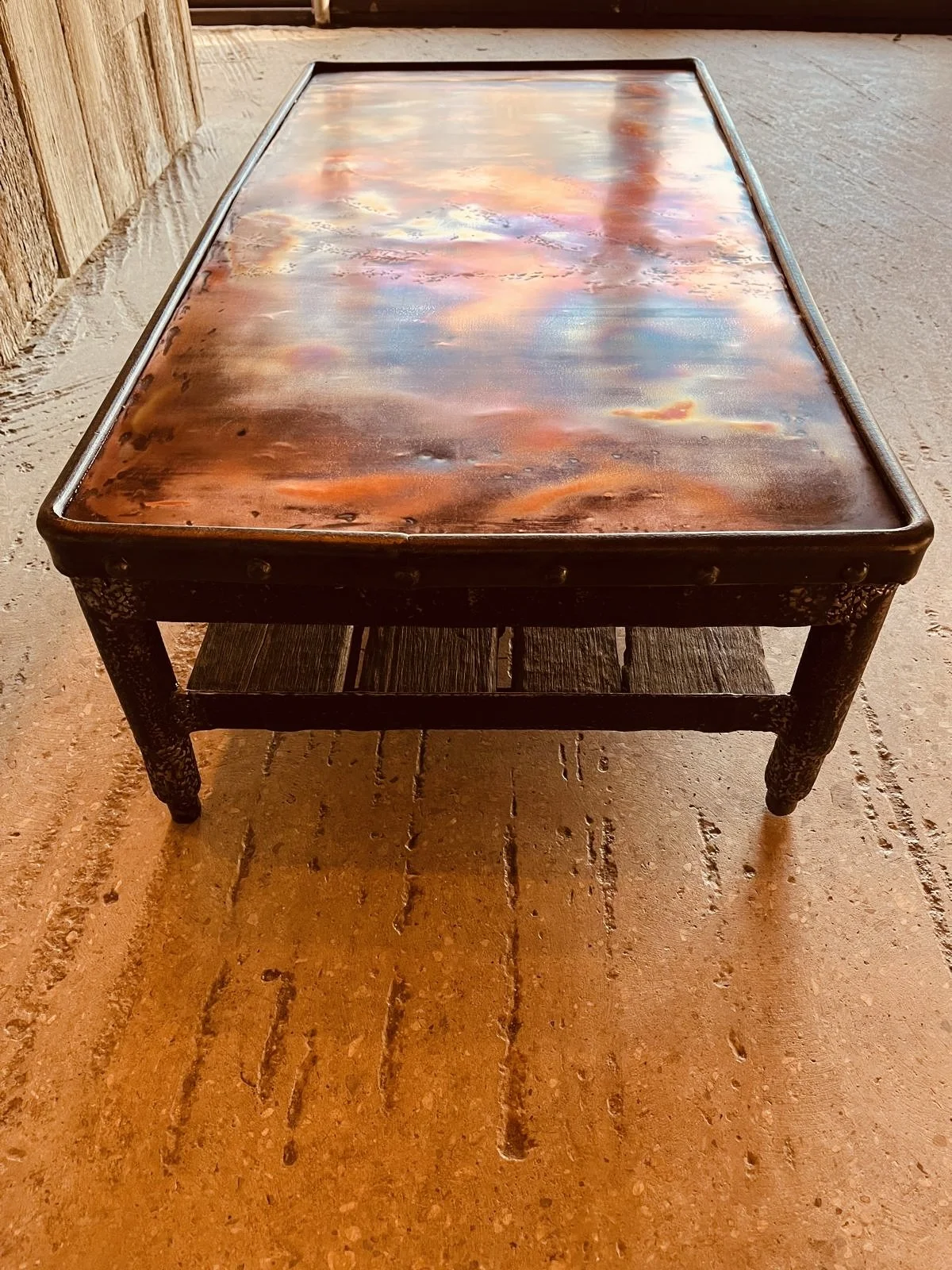 A rectangular wooden table with a glossy, painted surface reflecting a colorful sky of copper, positioned on a wooden floor.