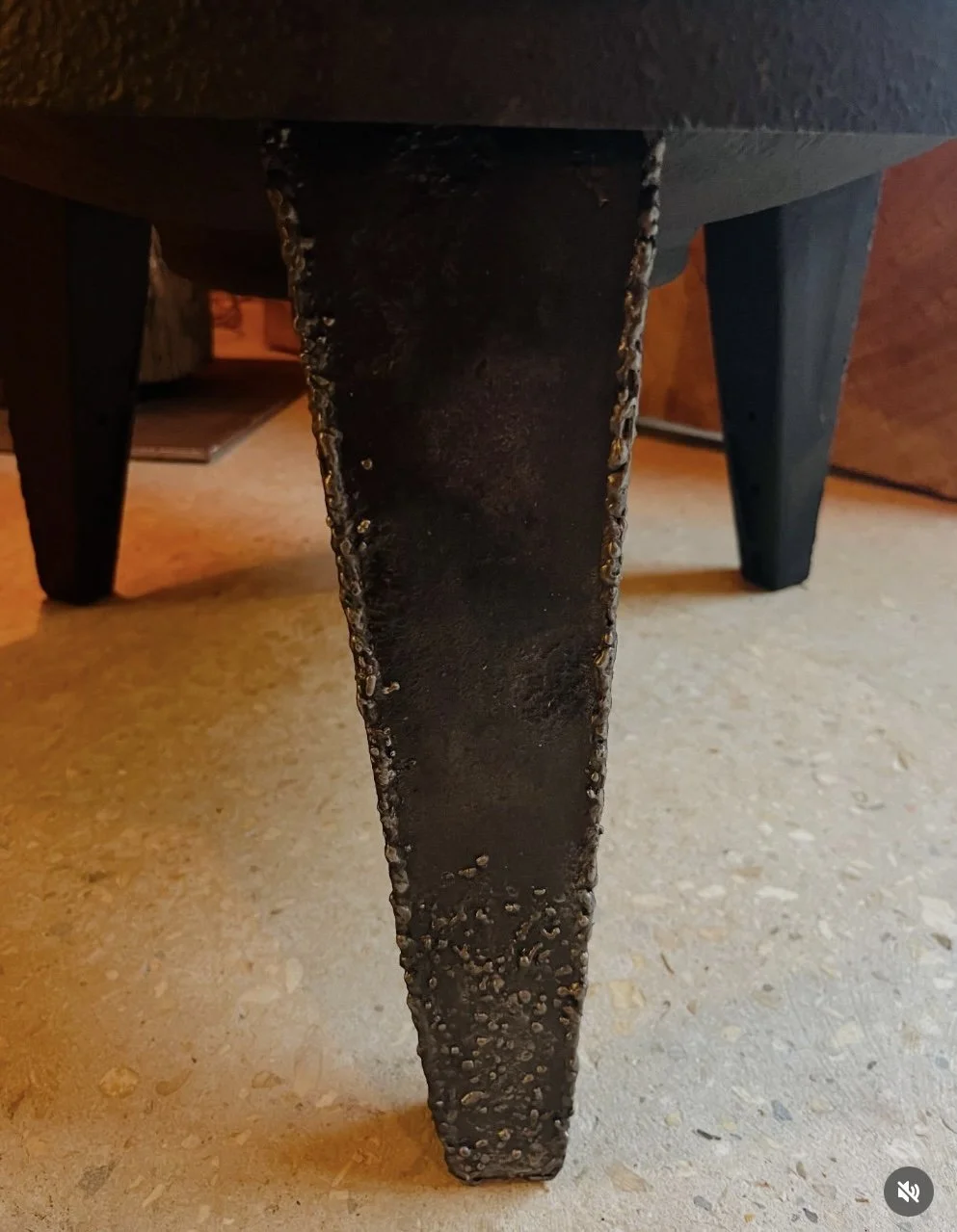 Close-up of a black wooden table leg with rough, uneven edges, showing signs of wear and chipping, on a tile floor.