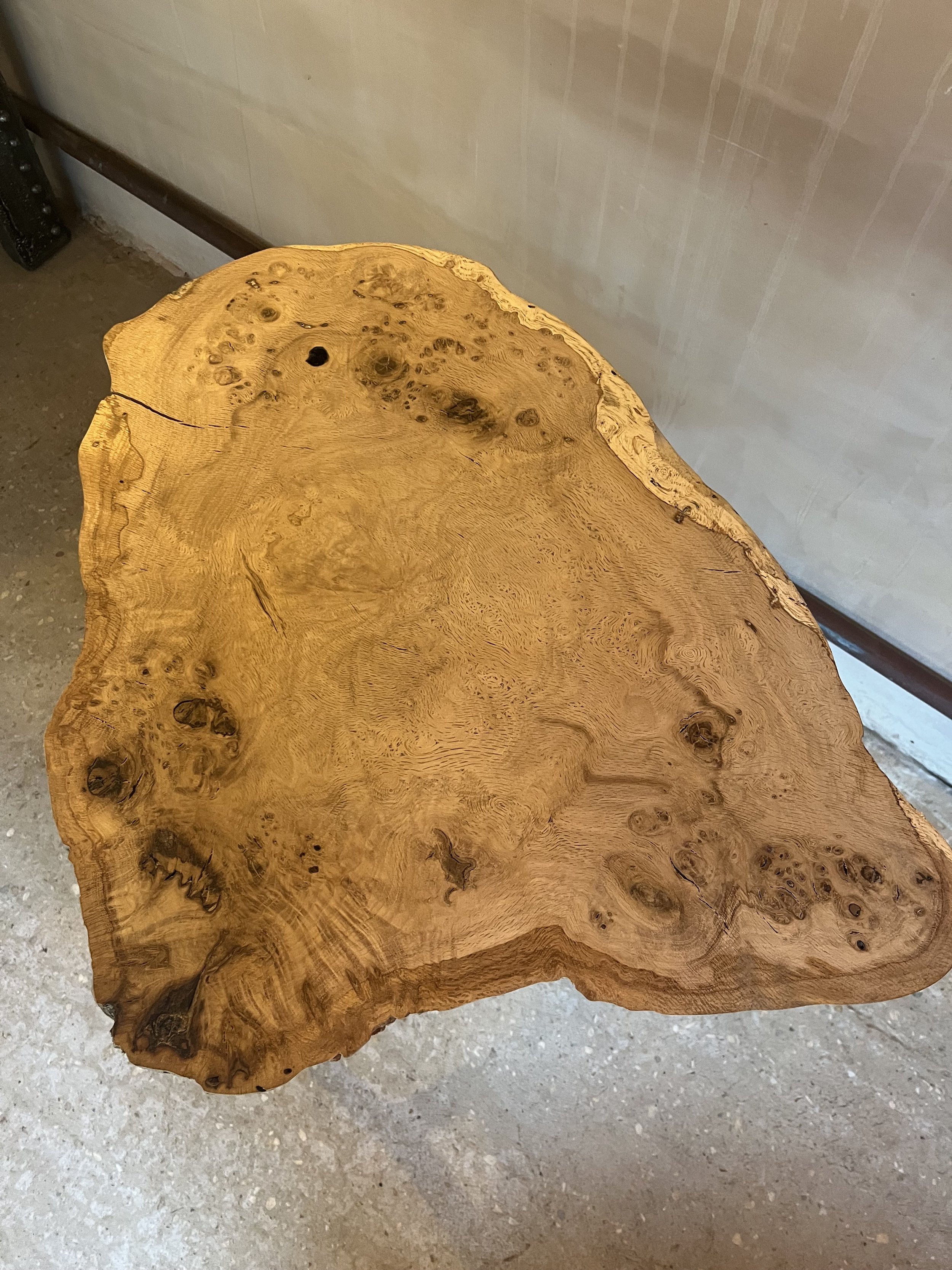 Wooden table made from a large, irregularly shaped piece of natural wood, showing knots and grain patterns.
