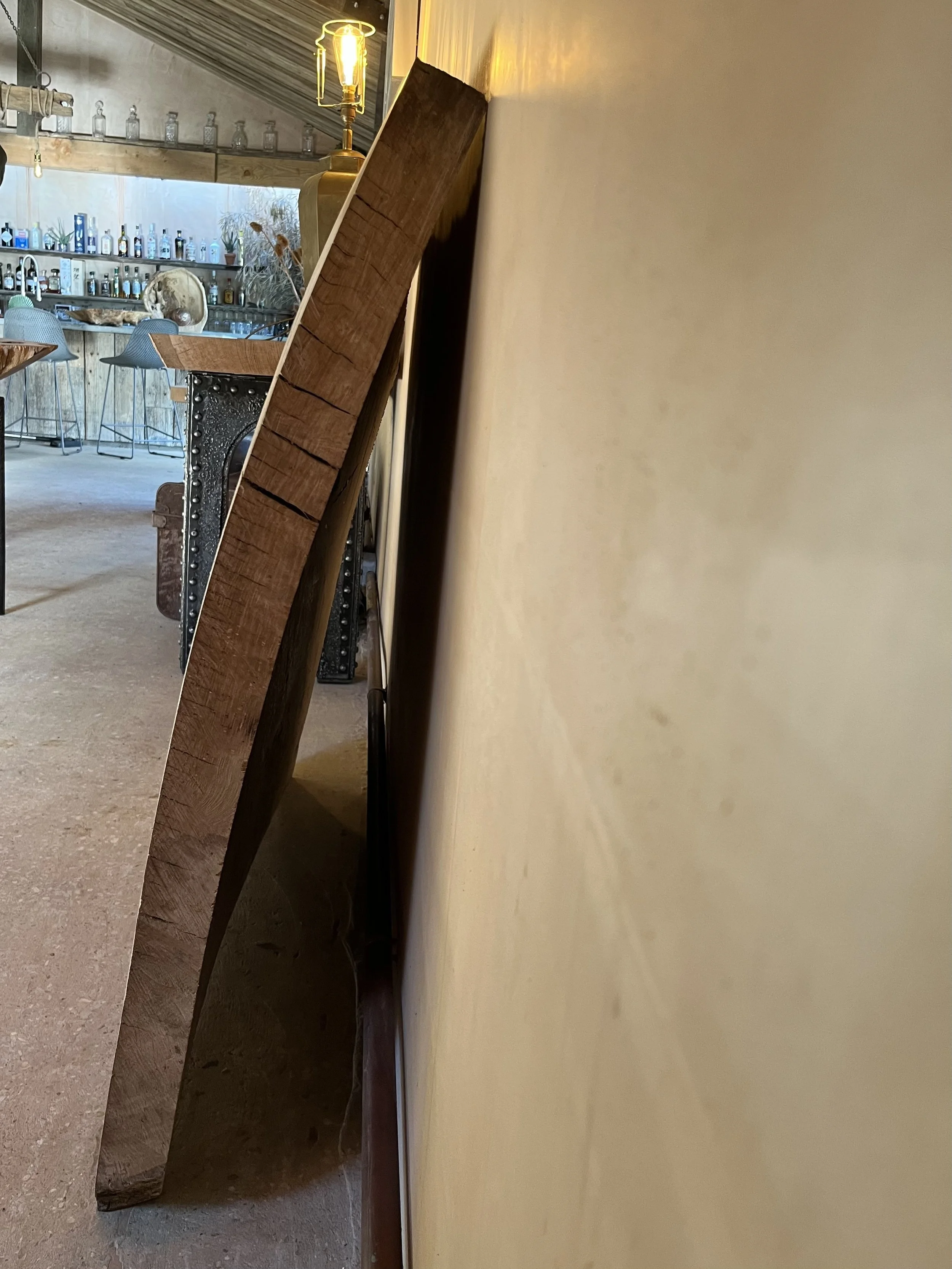 Unmounted flat-screen TV leaning against a beige wall in a room with a bar counter and chairs in the background, part of the TV's back is visible.