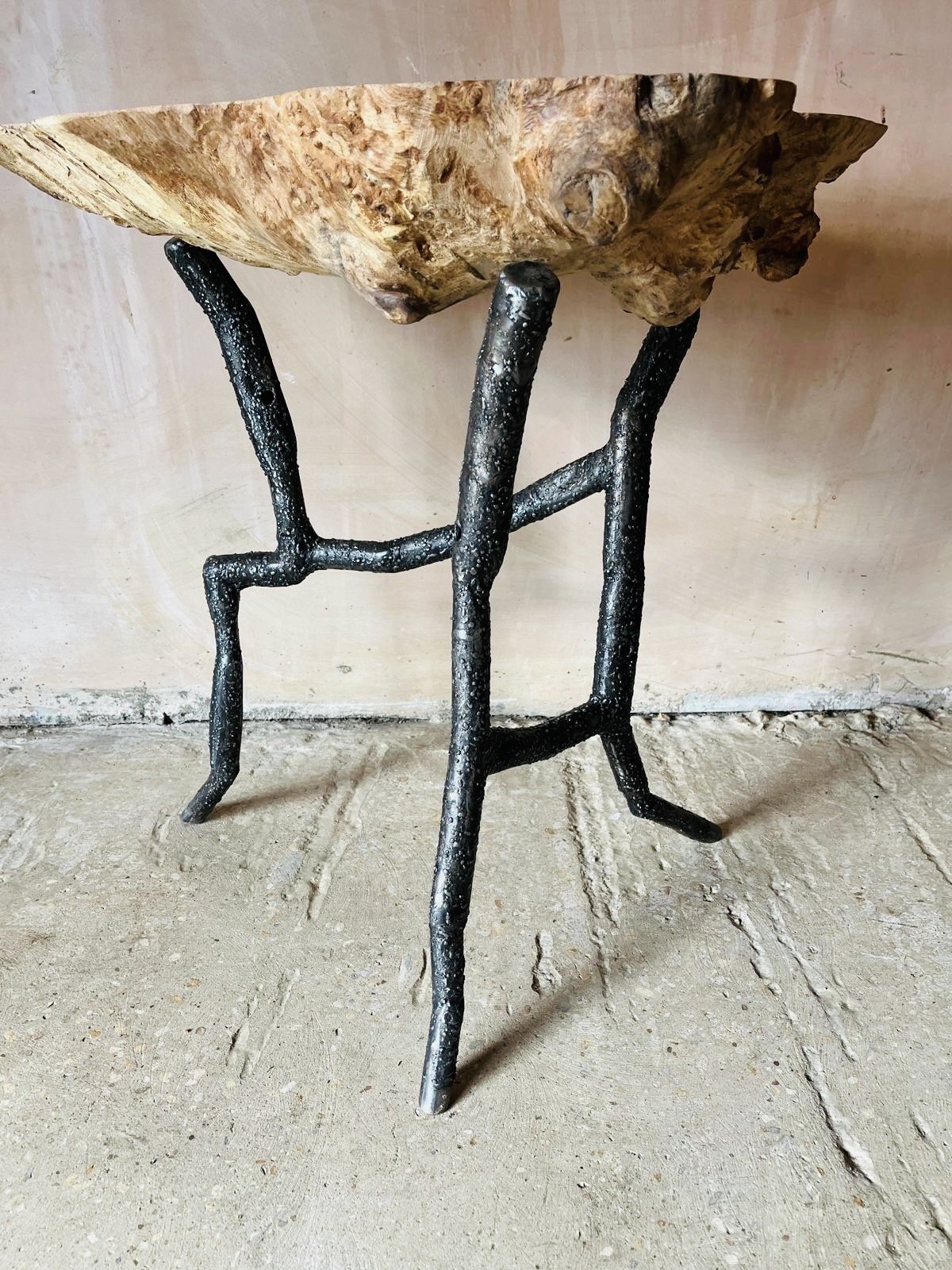 A side table with a natural wood bowl on top, featuring black metal legs designed to resemble tree branches.
