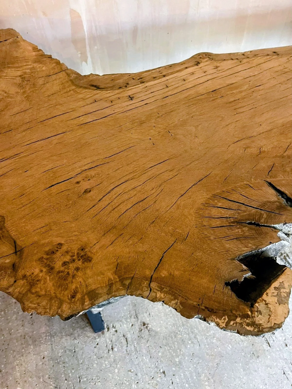Close-up of a large, natural wooden tabletop with visible wood grain, cracks, and knots, supported by black metal legs.
