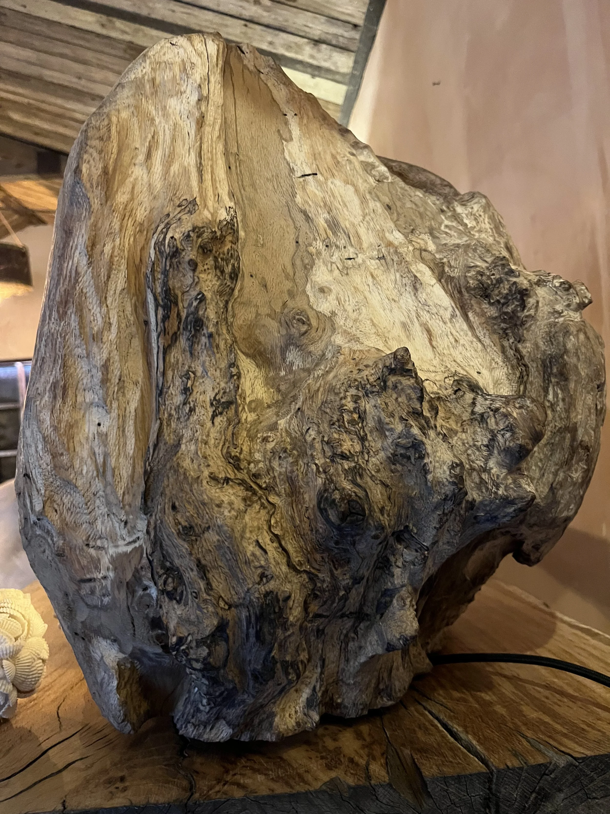 A large, irregularly shaped piece of driftwood with a weathered surface, placed on a wooden table inside a rustic interior.