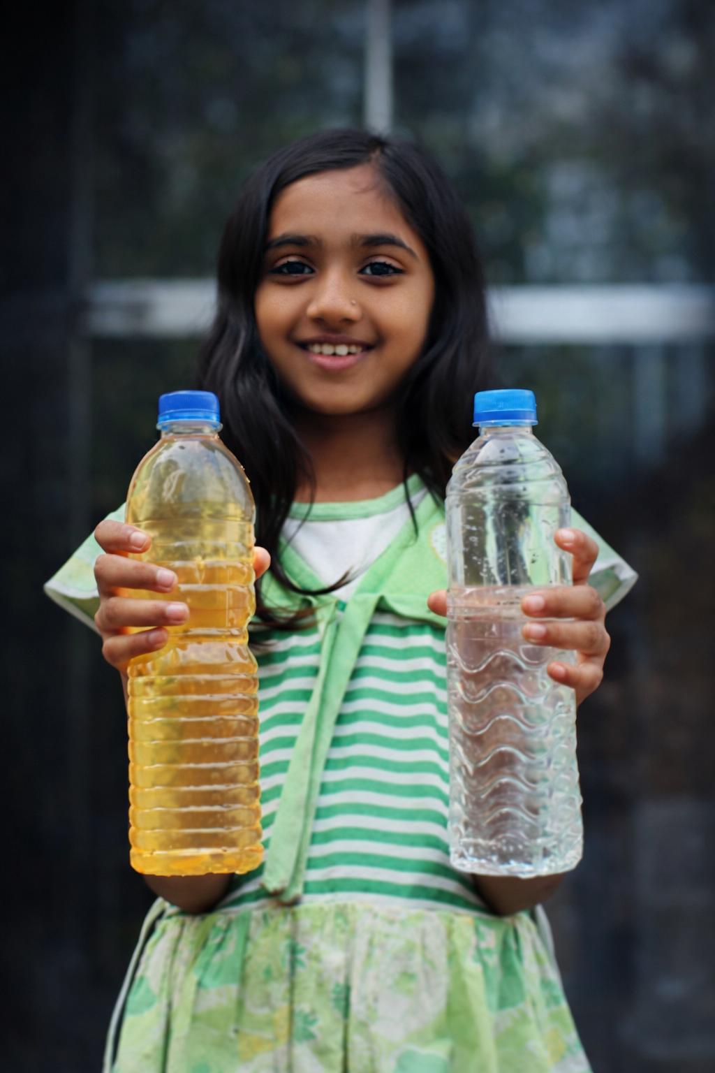 Girl holding iron contaminated water bottle on left and purified water bottle on right