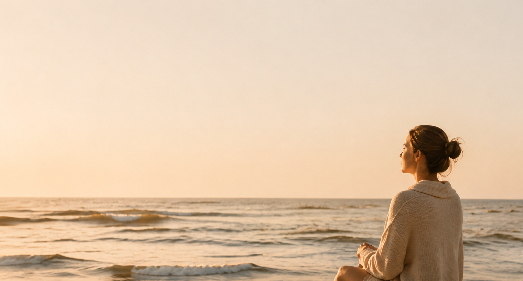 Een vrouw zit op het strand en kijkt naar de zee tijdens zonsondergang.