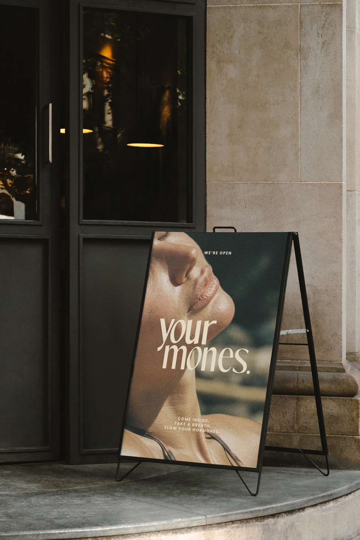 Een winkelbord met een close-up afbeelding van een vrouw die haar hoofd naar boven wentelt, met de tekst 'your mone' en een uitnodiging om naar binnen te komen en adem te halen, en je hormonen te laten stromen.