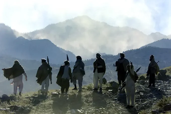 A group of nine people hiking on a mountain trail with misty mountain peaks in the background.