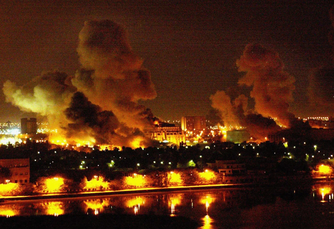 Nighttime Baghdad with large fire and thick black smoke rising from multiple buildings.