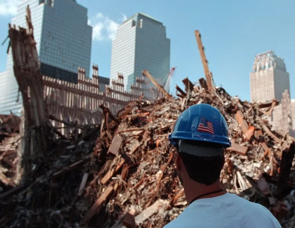 Person wearing a blue construction helmet looking at the ruins of the World Trade Center after the 9/11 attacks in New York City.