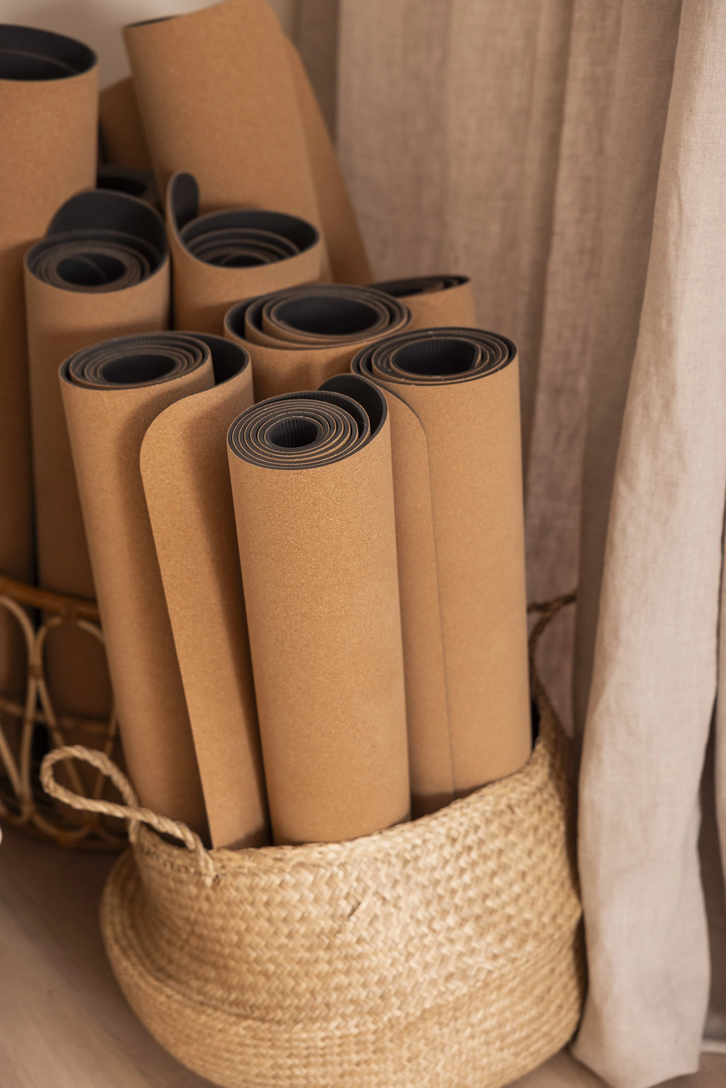 Opgerolde yogamatten in een gevlochten mand naast beige gordijnen in de yogastudio bij Roots Yoga in Deurne.