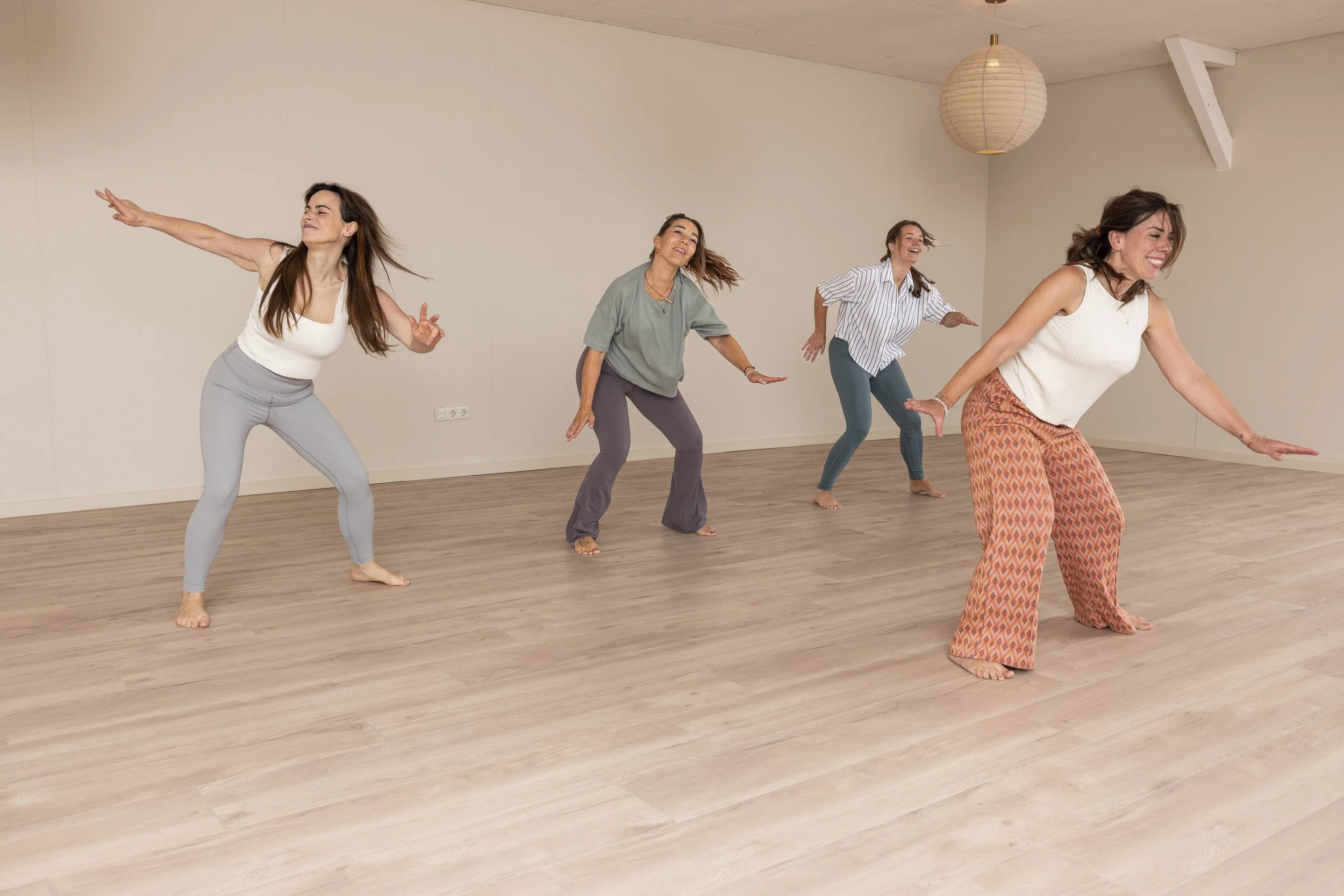 Vier vrouwen oefenen yoga of dans in een ruime studio met lichte houten vloer en minimalistische inrichting bij Roots Yoga in Deurne.