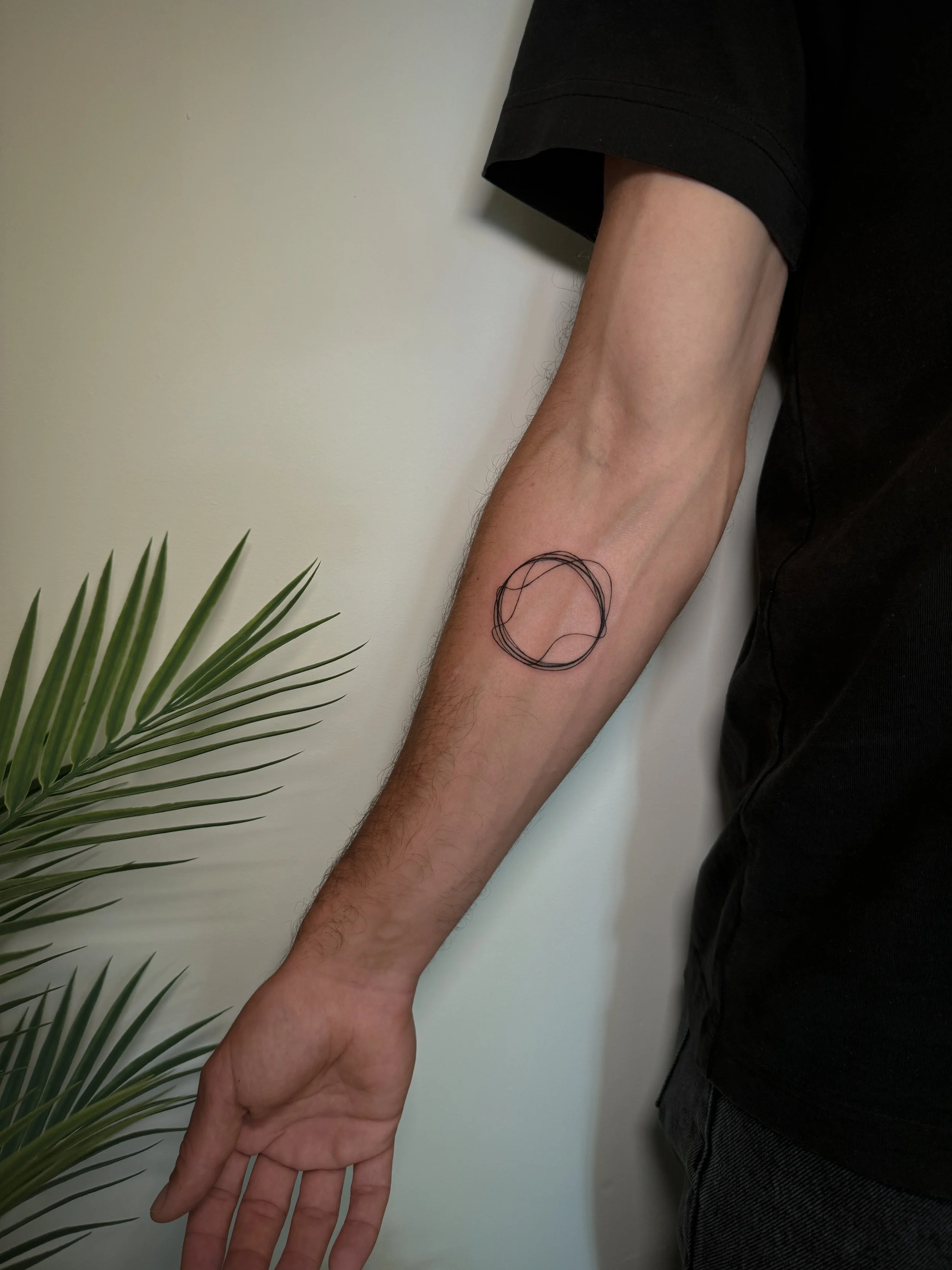 A person's arm extended downwards, revealing a fineline tattoo of three overlapping circles on the inner forearm.