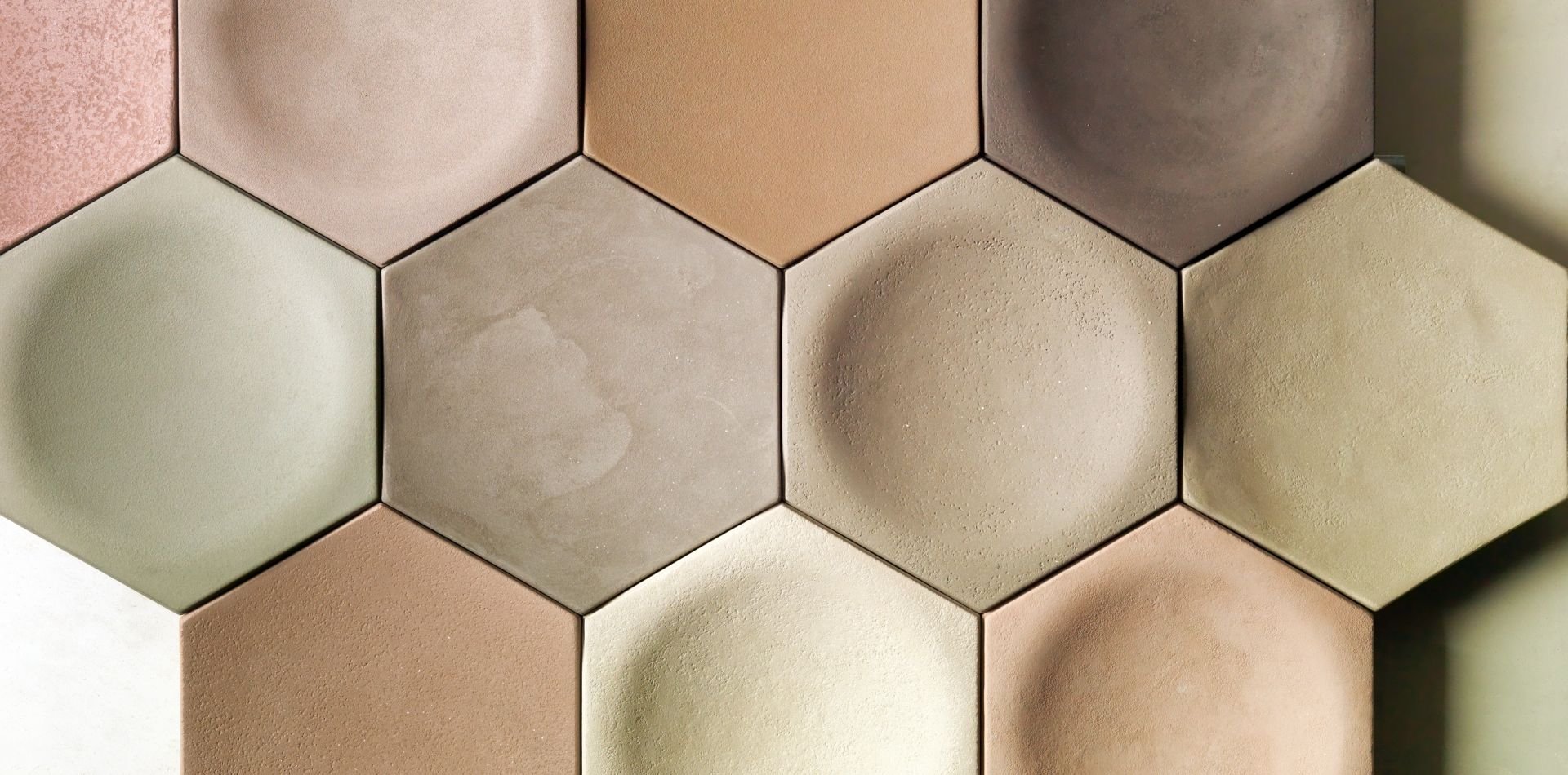 Close-up of hexagonal tiles with matte and textured finishes in beige, tan, pink, and green tones.