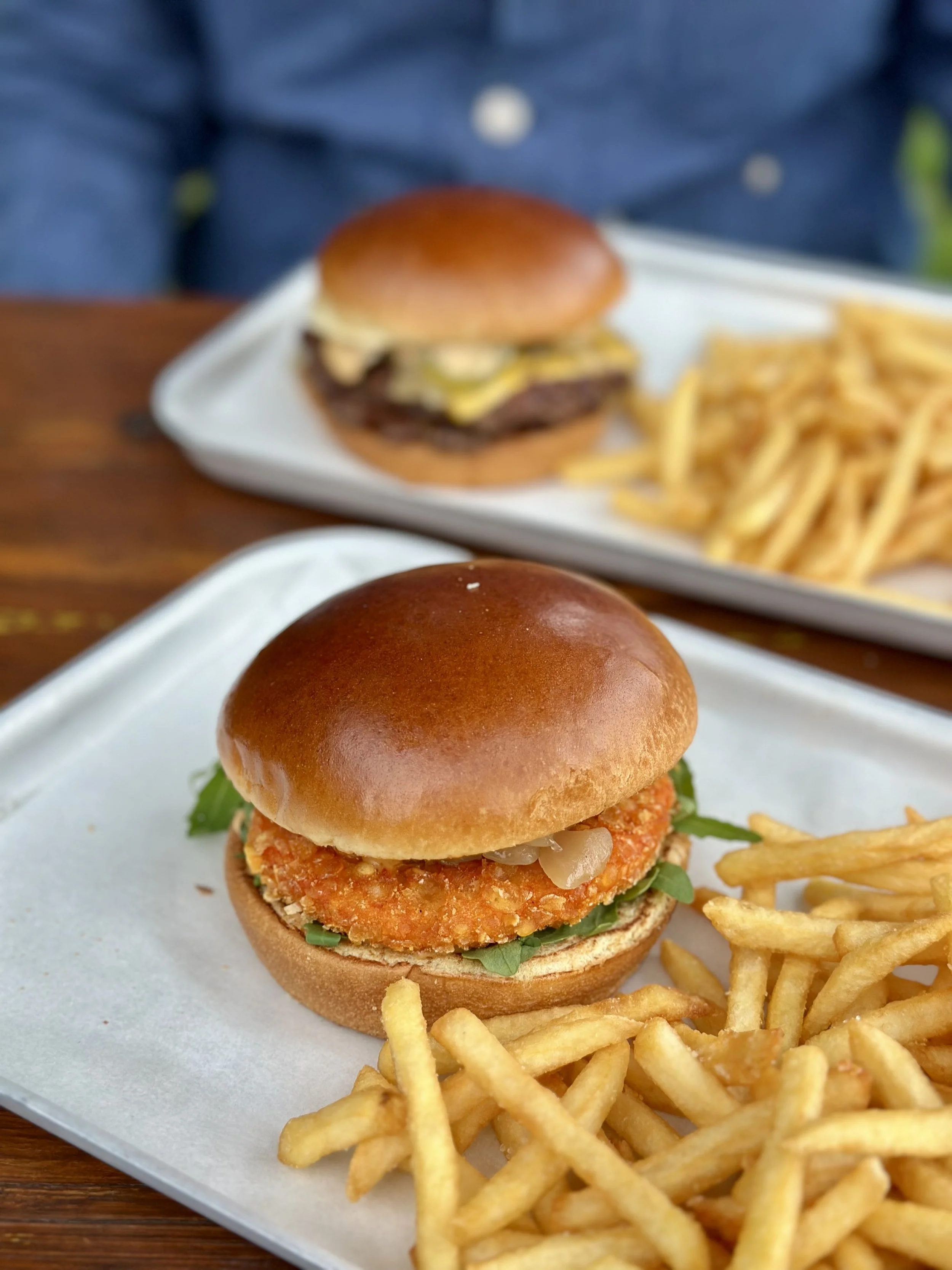 Ein Burger mit paniertem Hähnchenfilet, Salat, Zwiebeln und einer Brötchen, dazu Pommes Frites, auf einem weißen Teller.