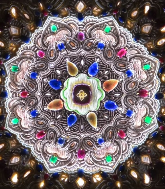A colorful, ornate, and symmetrical glowing design with vibrant teardrop-shaped accents and intricate patterns resembling a decorative stained glass or crystal art piece.