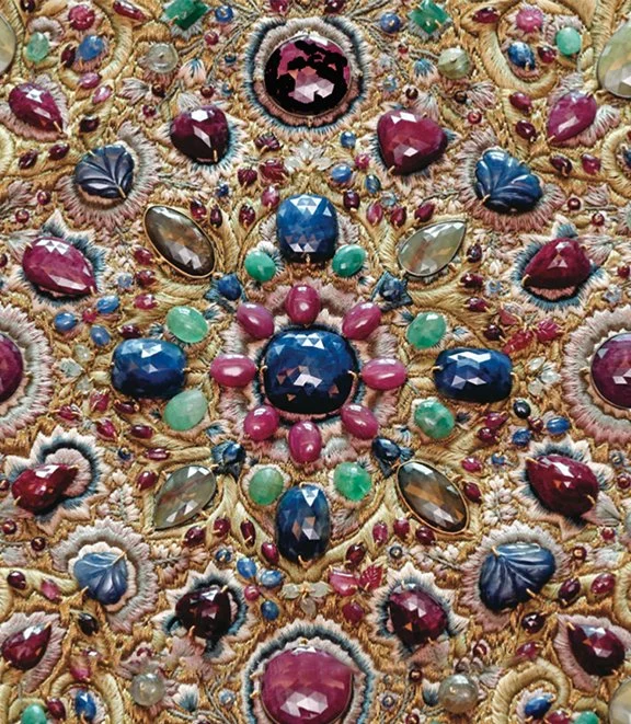 Close-up of an ornate, jeweled embroidery with colorful gemstones, pearls, and intricate gold threadwork.