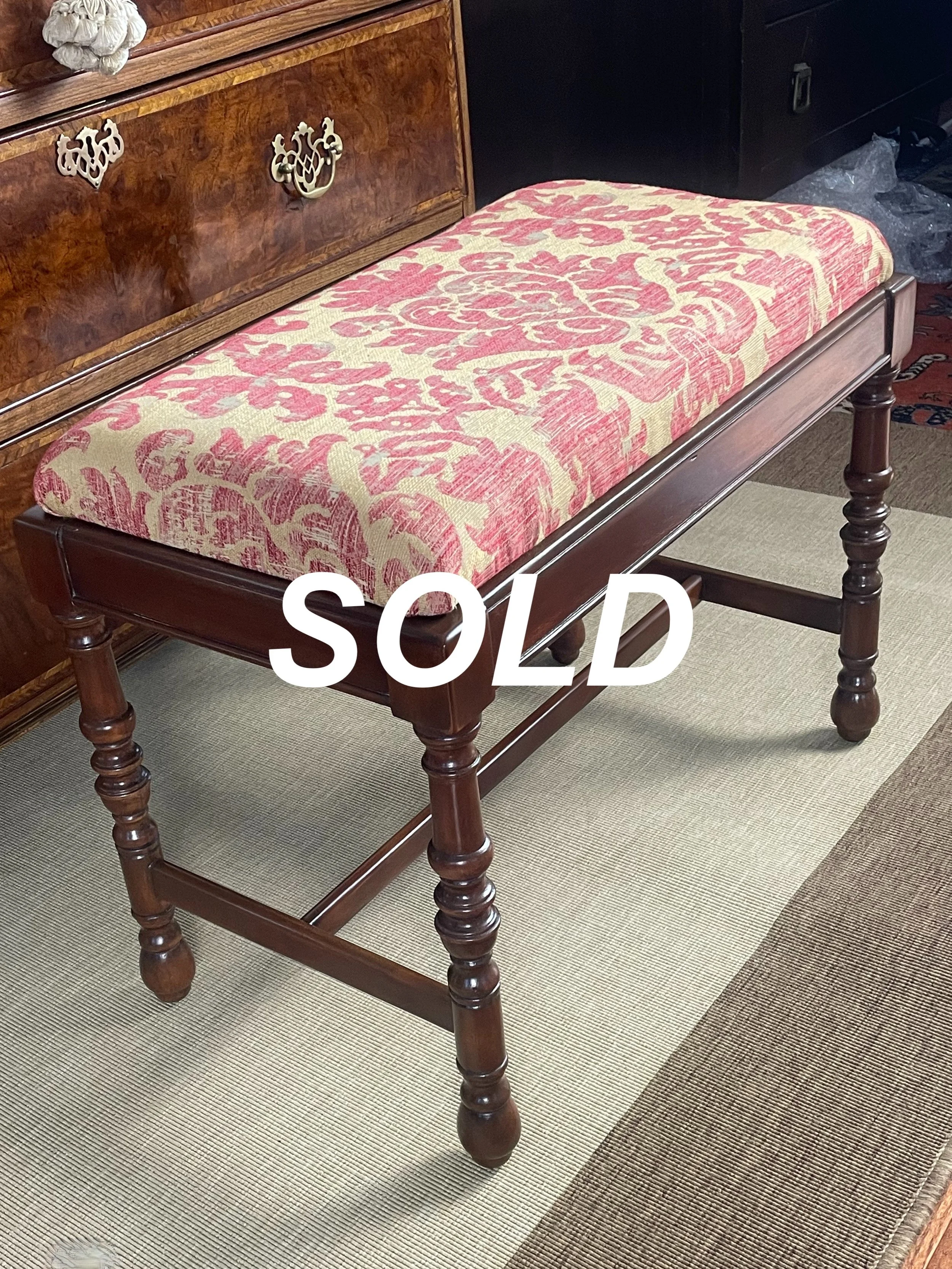 A wooden bench with a floral patterned cushion, standing on a carpeted floor with multiple shades of brown and beige, adjacent to a dark wooden cabinet.