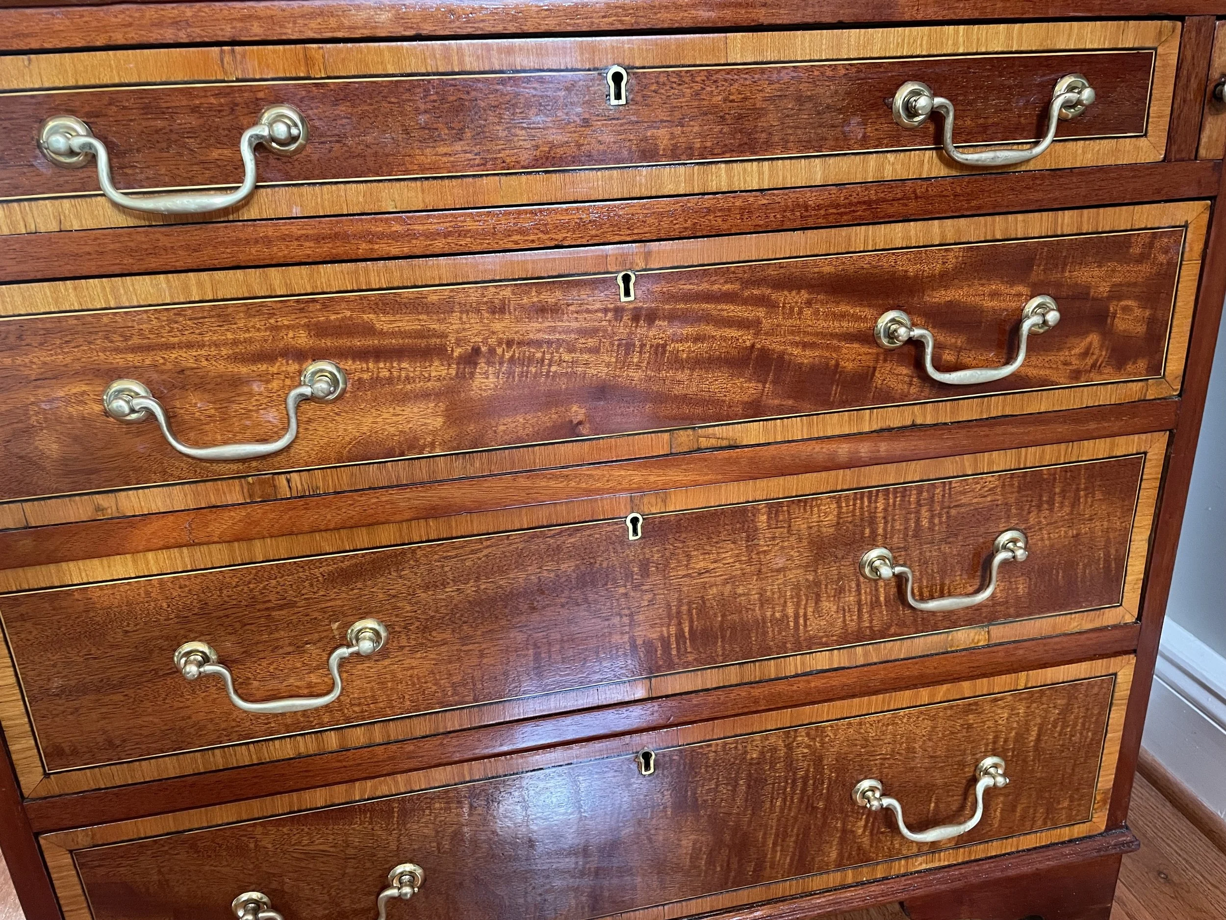 Classic swan-head brasses over a patterned mahogany field and satinwood edge banding, outlined in black and light stringing. 