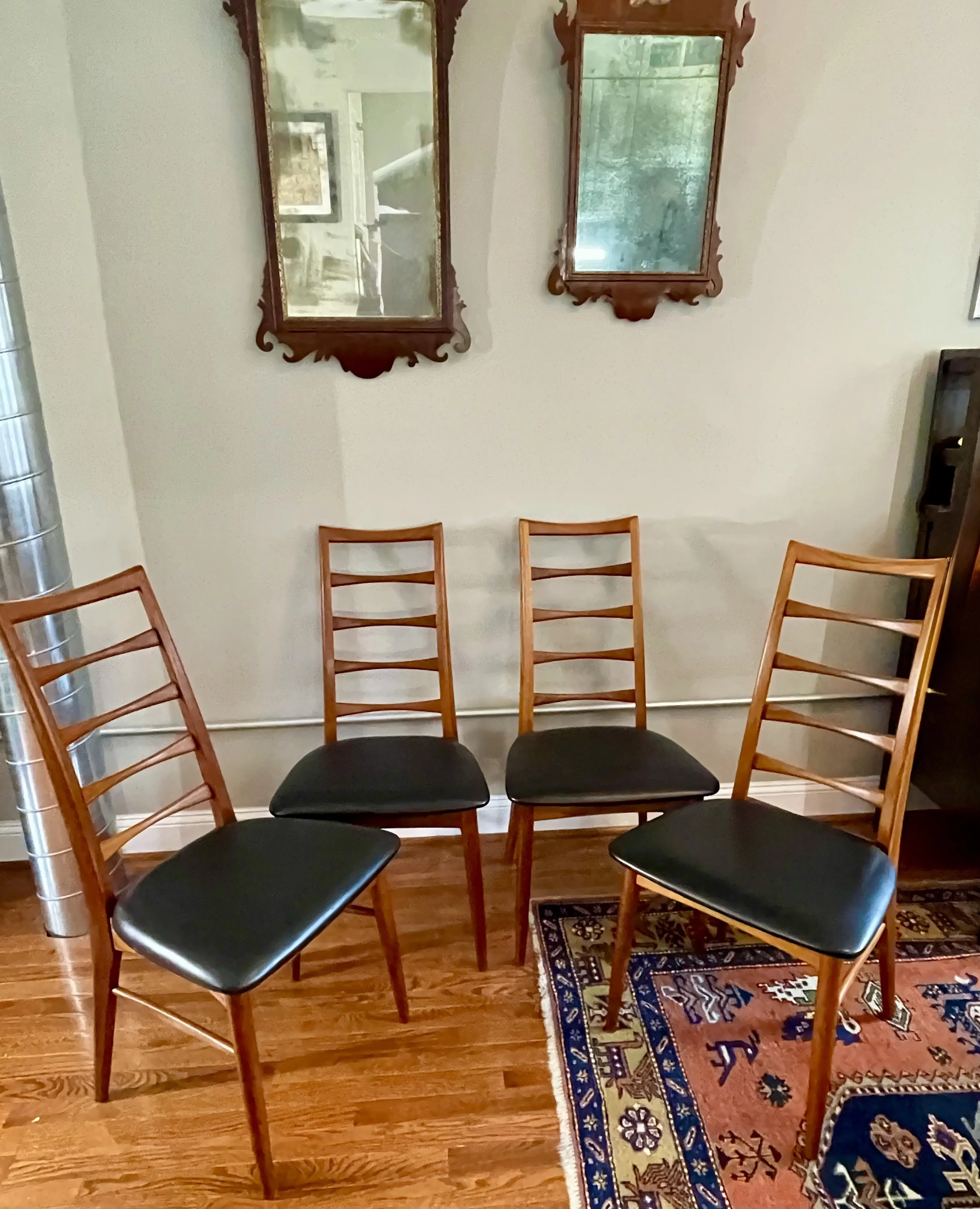 Four wooden chairs with black seats arranged in a semi-circle in front of a wall with two decorative mirrors.