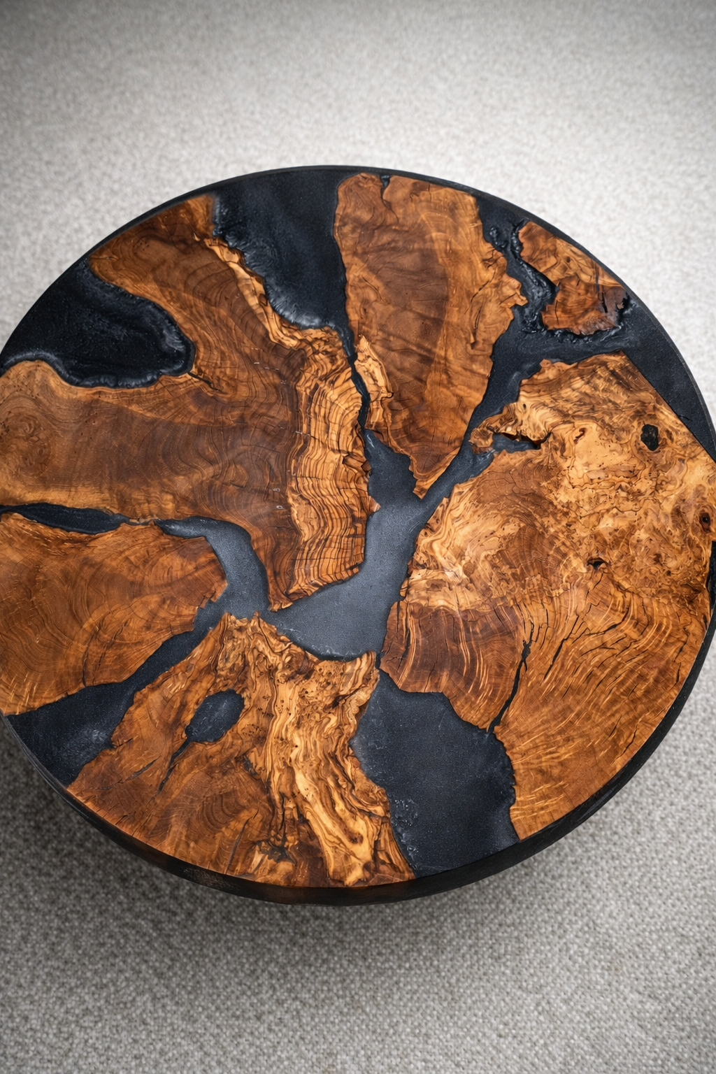 A round wooden table with a black border, featuring a design that resembles a map or abstract artwork, with intricate wood grain patterns and dark inlays.