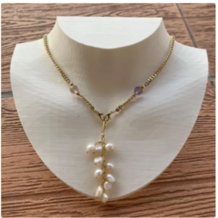 Collier avec pendentif en perles blanches et chaînette dorée, exposé sur un collier en mannequin en bois.