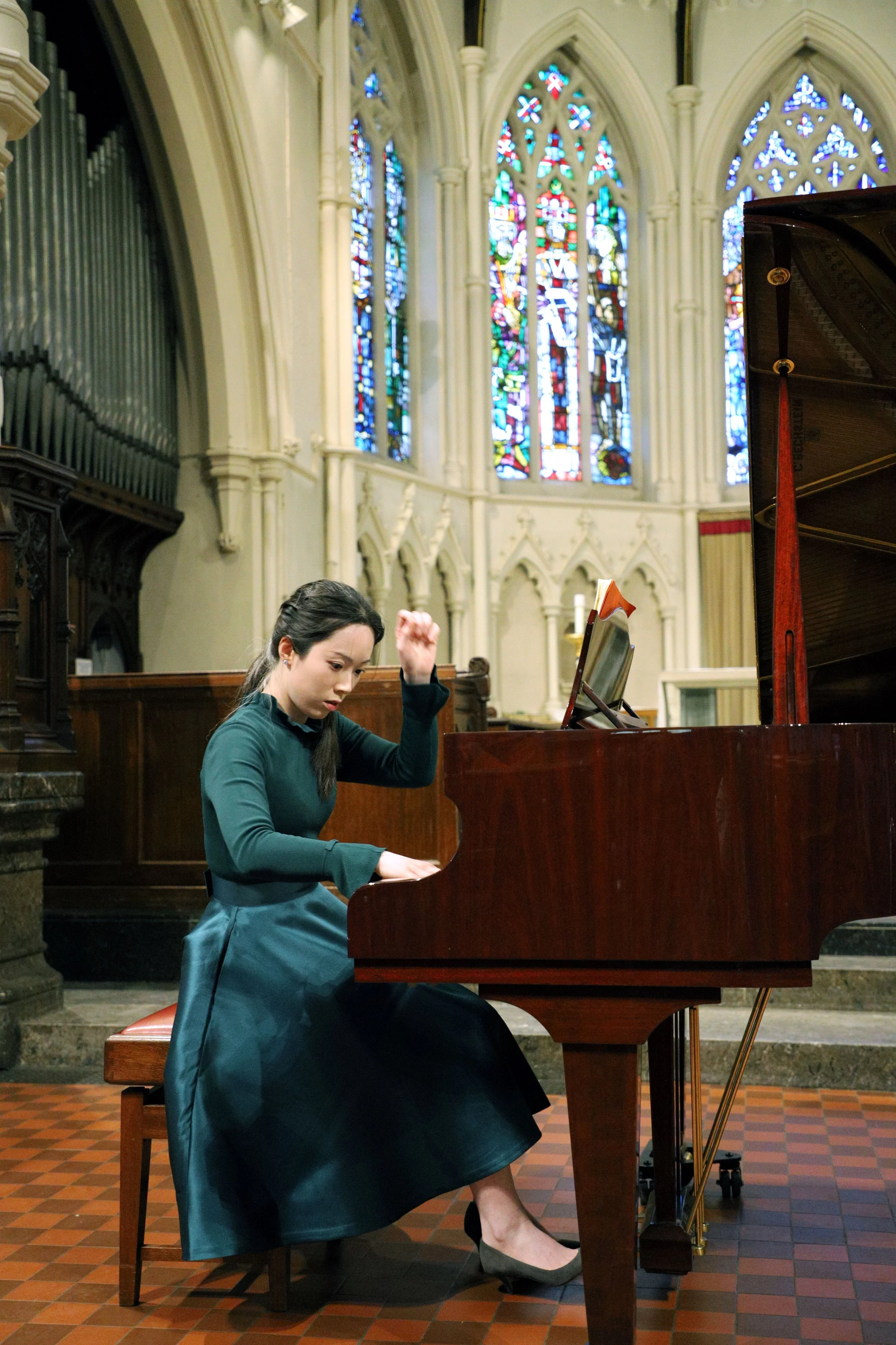 Jessica Wu, a young woman, playing a grand piano inside a church with stained glass windows.
