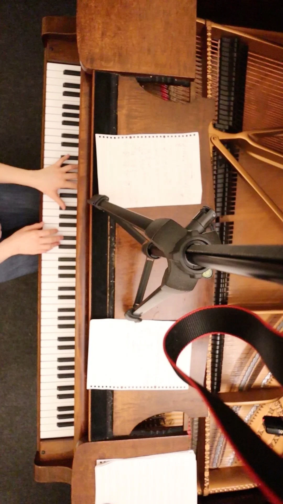 Jessica Wu, a young woman, playing a wooden upright piano with sheet music and a microphone on a stand in front.