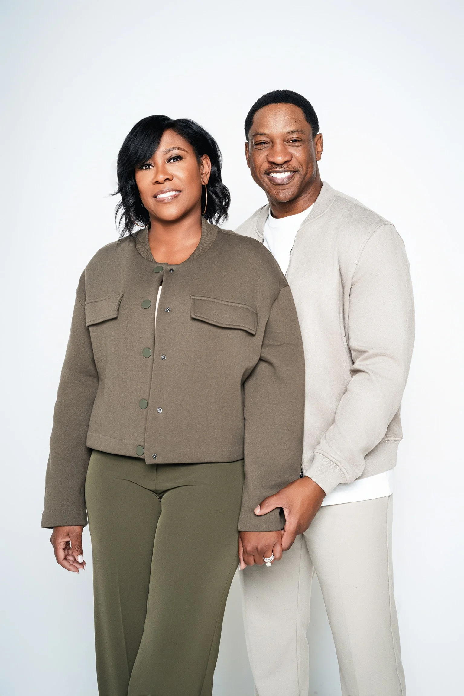 A smiling African American couple standing close together, holding hands, with a plain white background.