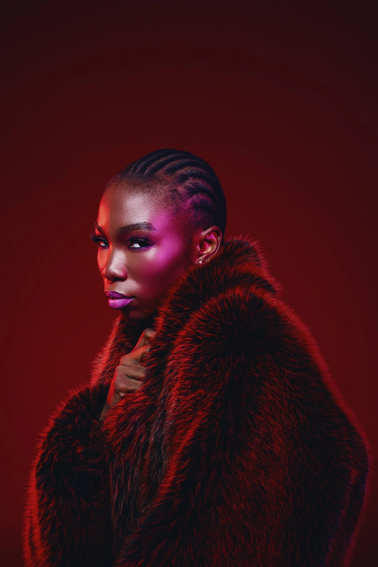 A woman with styled hair wearing a fur coat against a dark red background.