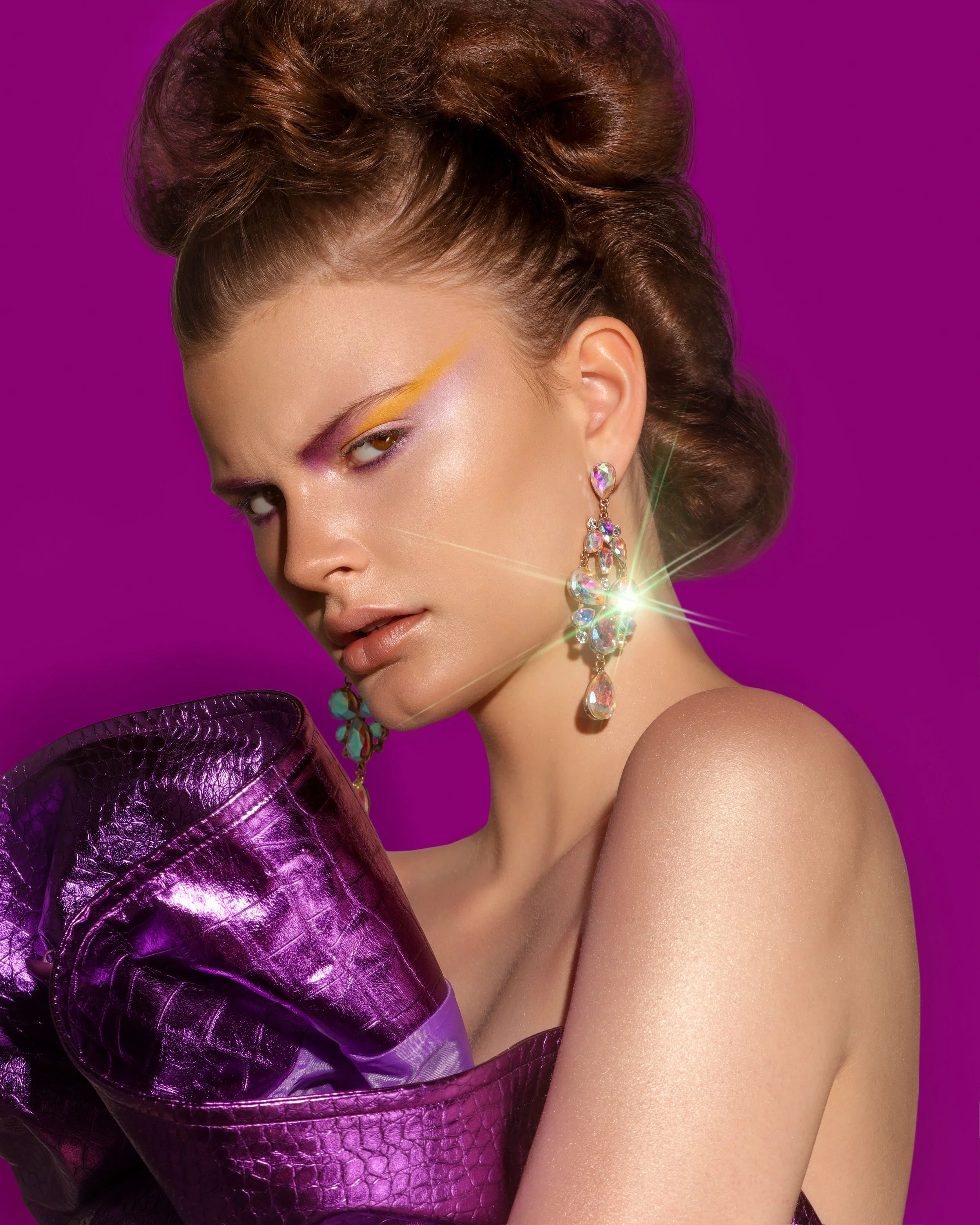 A woman with styled brown hair, wearing large, sparkly earrings, and a purple textured dress, poses against a solid purple background with a focused expression.