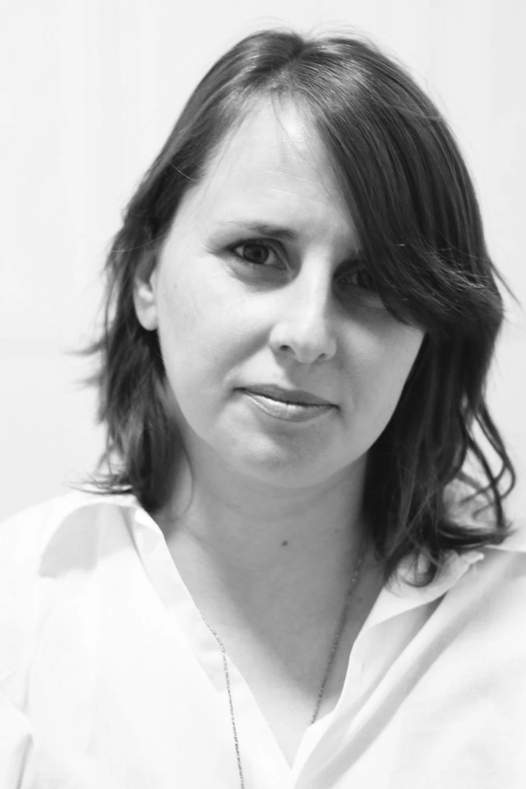 Black and white portrait of a woman with shoulder-length hair, wearing a white blouse and a necklace, looking at the camera with a slight smile.