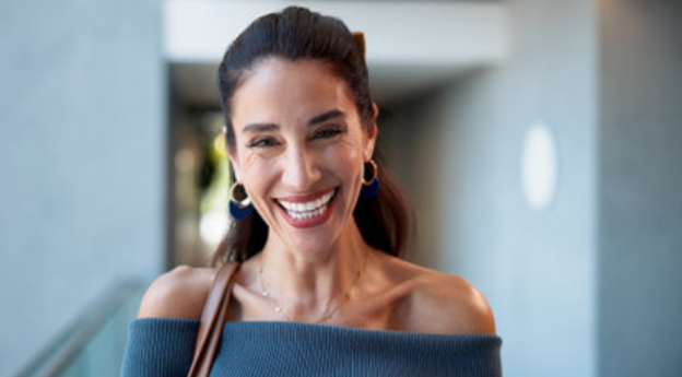 A woman smiling and looking happy, standing outdoors near a building.