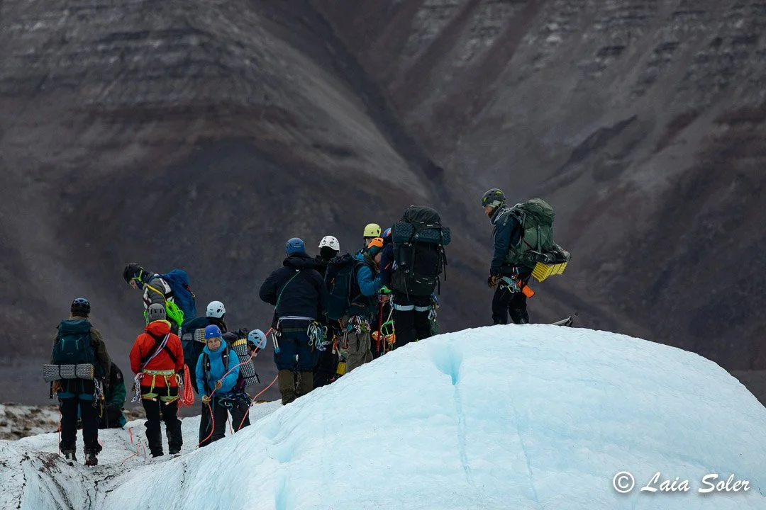 A group of mountaineers with backpacks and climbing gear on a glacier, preparing to navigate the crevassed area.
